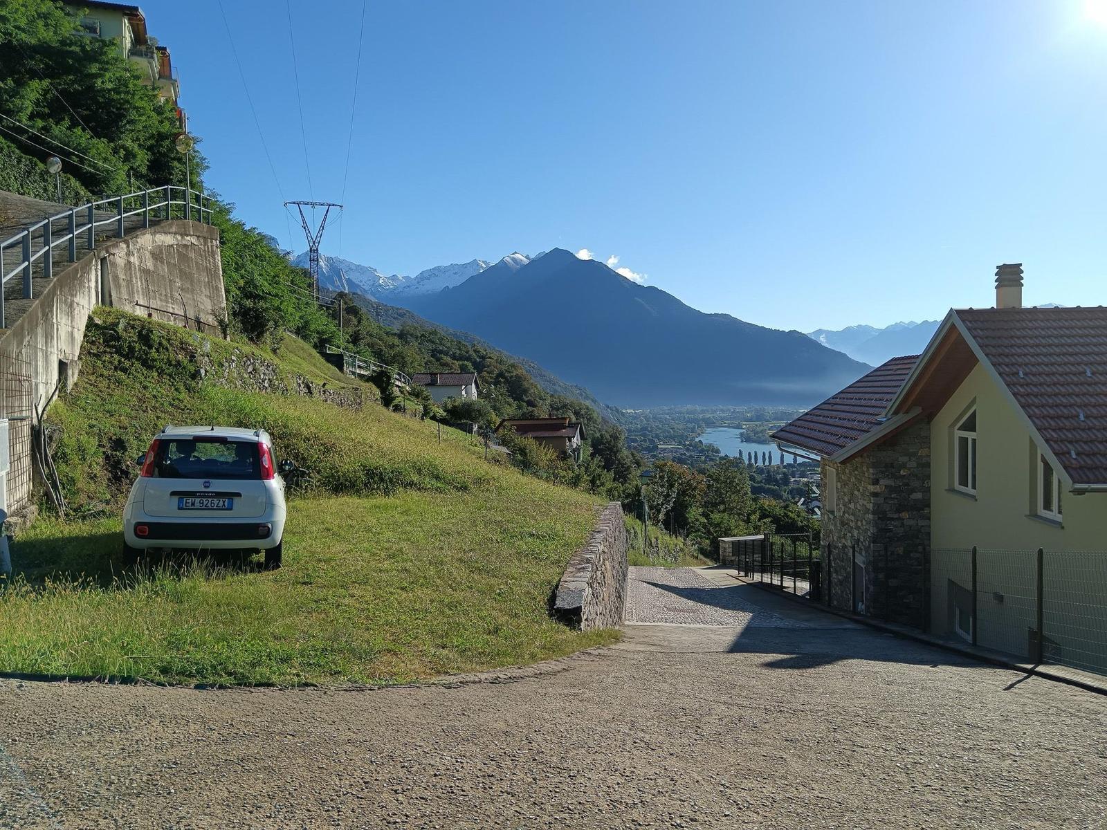 Haus mit Blick auf Berg und See, gepflasterter Weg und parkender Wagen.