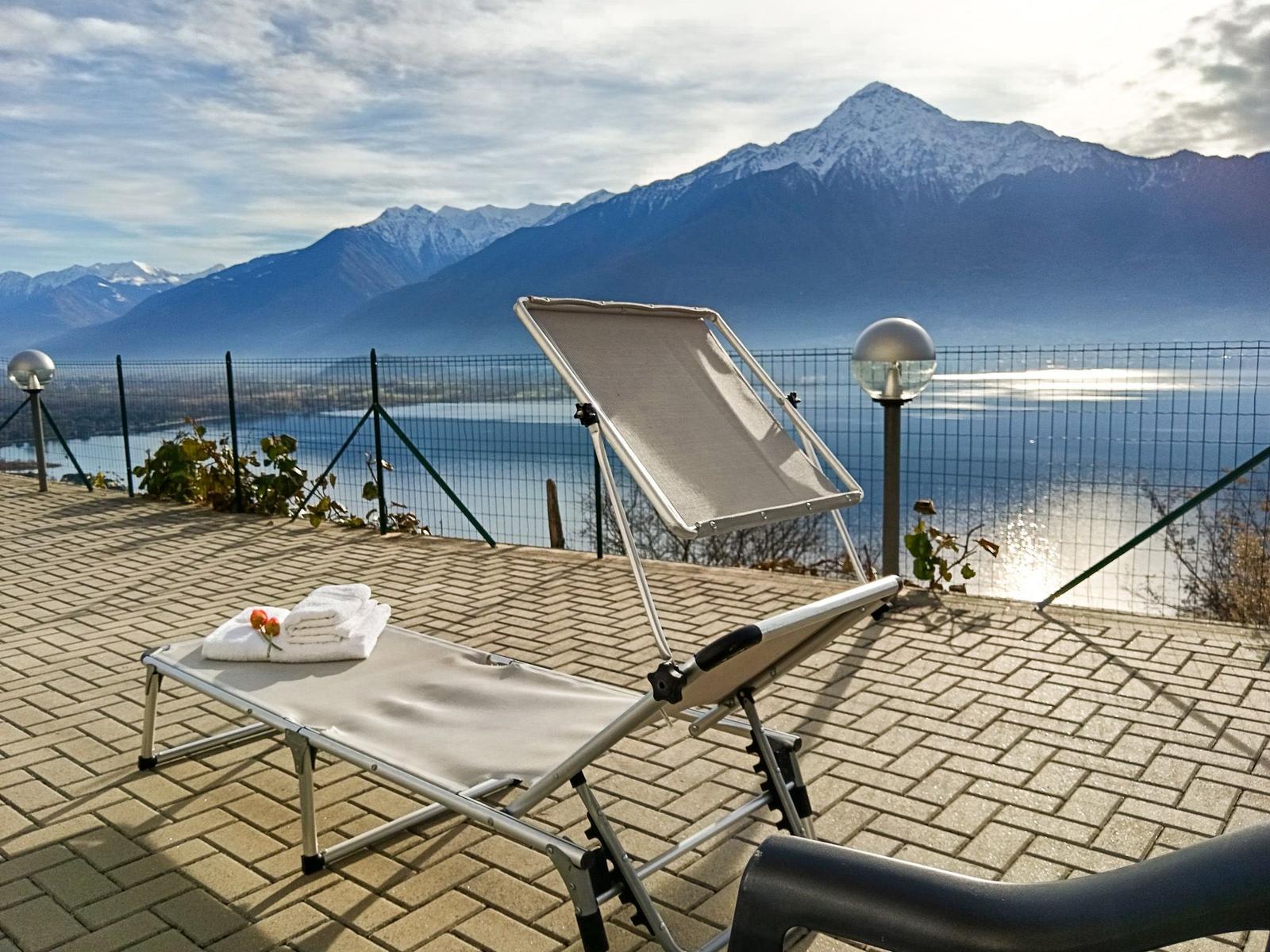 Liegestuhl auf Terrasse mit Blick auf See und Berge.