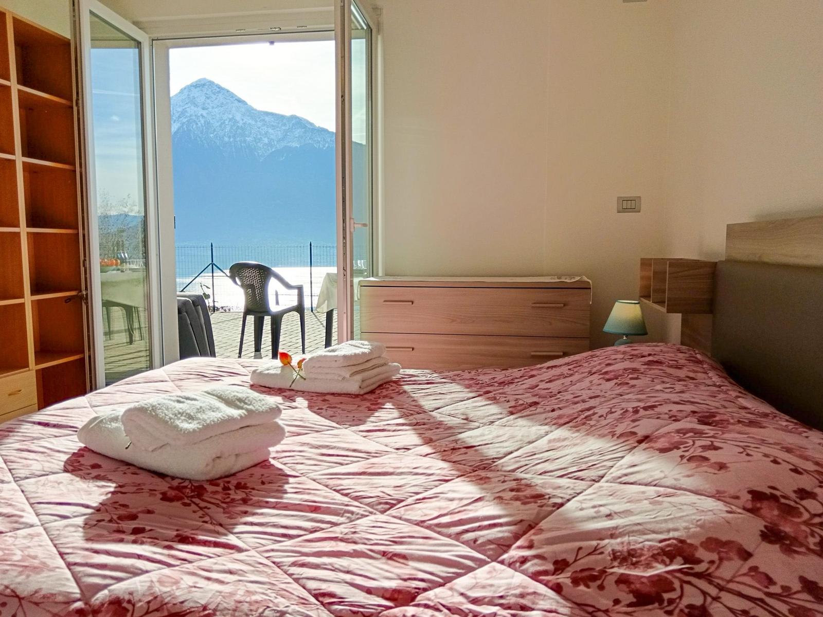 Schlafzimmer mit Blick auf Berg und See. Bett mit Handtüchern, Schrank und Nachttisch.