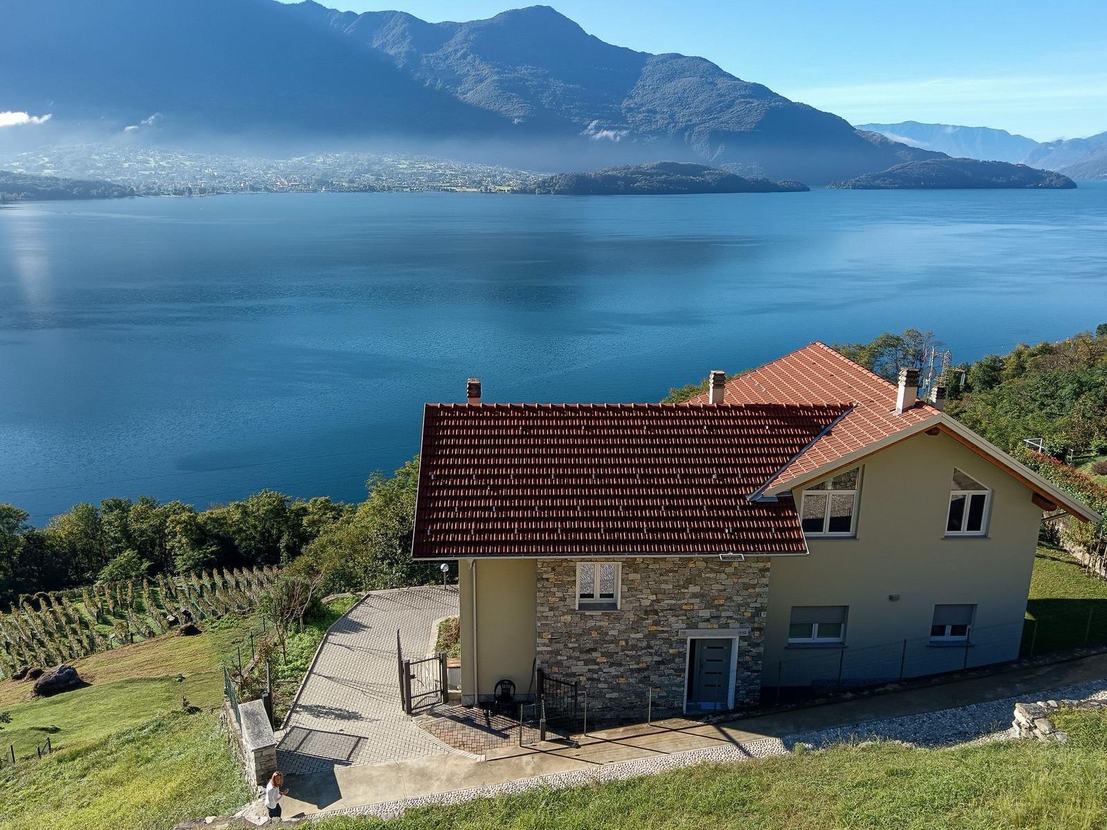 Haus mit Blick auf See und Berge. Terrasse, Garten und Zufahrt sichtbar.