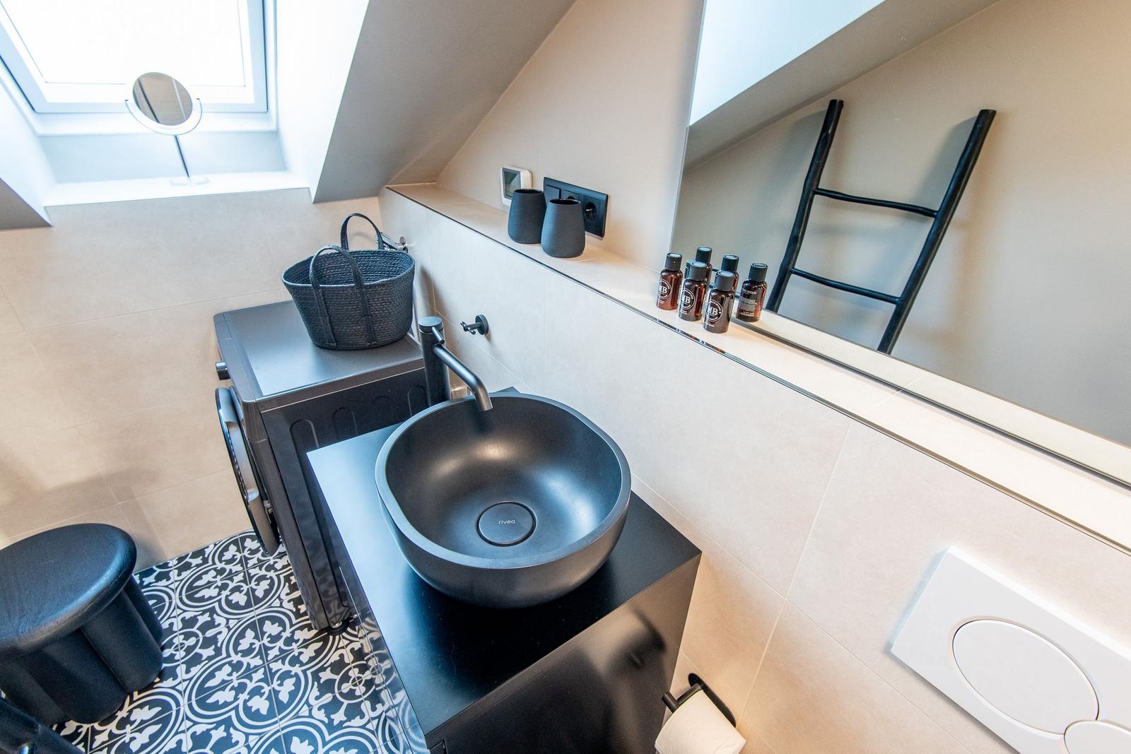 Dusche mit Waschbecken, Spiegel und Duschvorhang. Fliesenboden und Dachfenster.