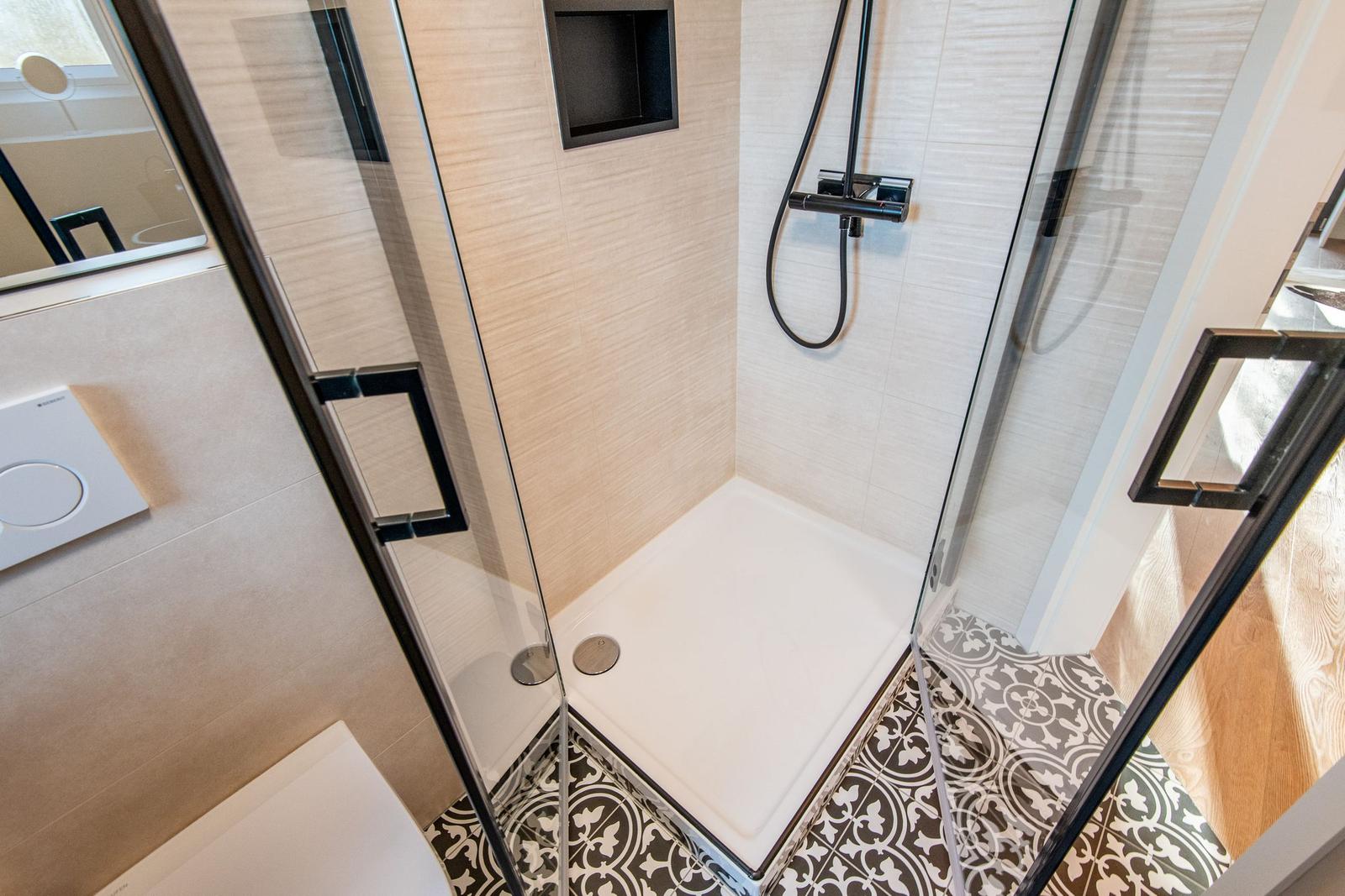 Dusche mit Glaswand, schwarzen Armaturen und Mosaikfliesen am Boden.