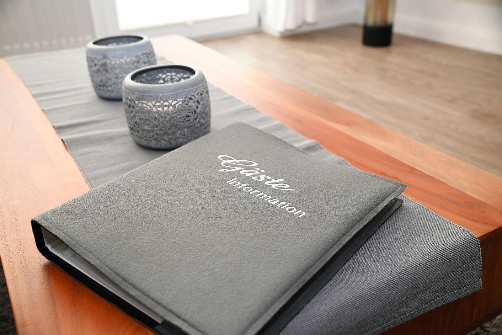 Gästeinformation liegt auf einem Holztisch mit grauer Tischdecke und zwei dekorativen Schalen.