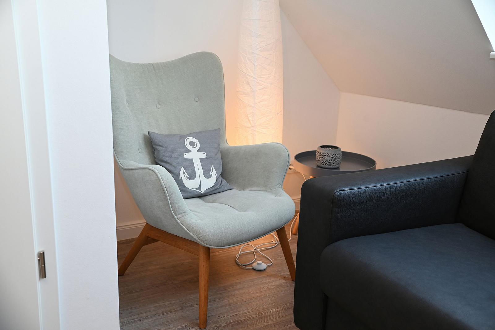 Ein grauer Sessel mit Kissen und eine schwarze Couch stehen in einem Raum mit Holzboden.