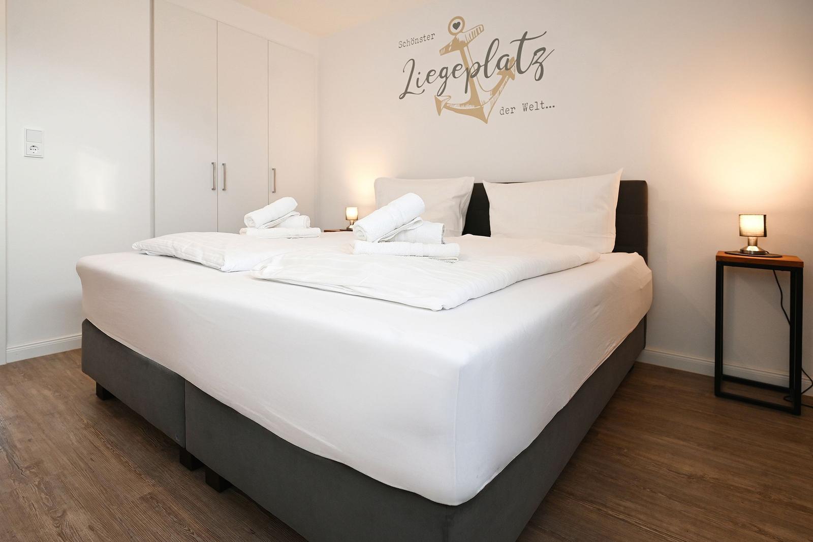 Schlafzimmer mit Doppelbett, weißen Laken und Wanddekoration mit Anker.