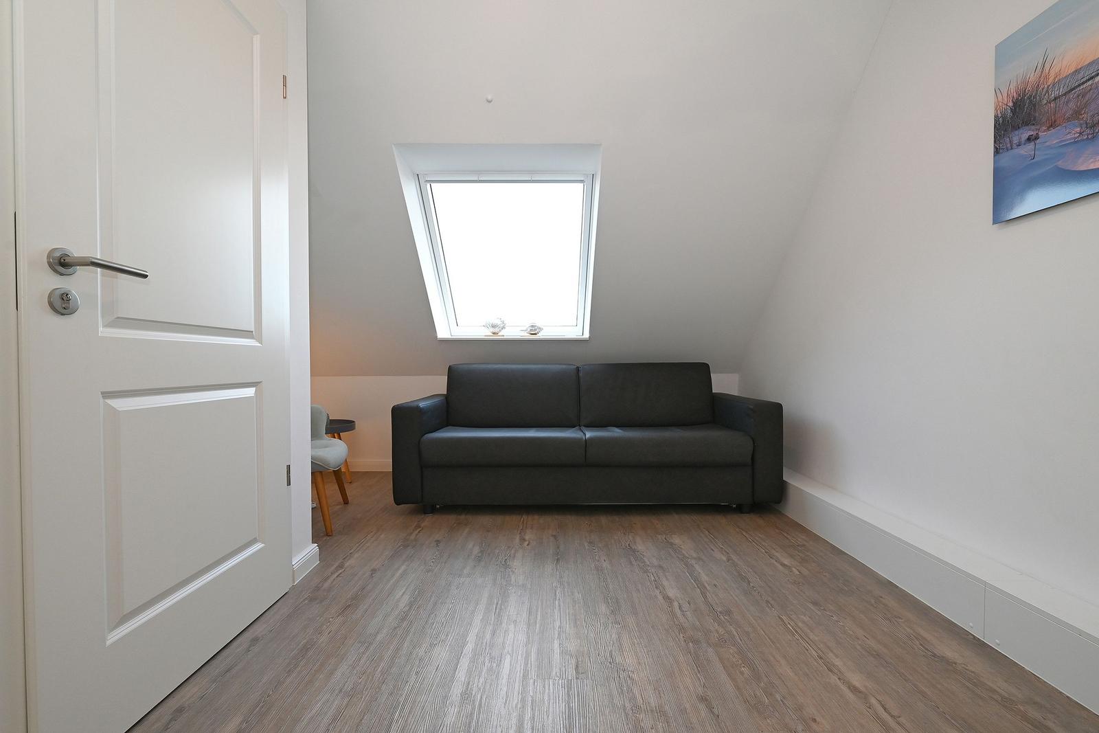 Ein Raum mit grauem Sofa, Holzboden und Dachfenster. An der Wand hängt ein Bild.