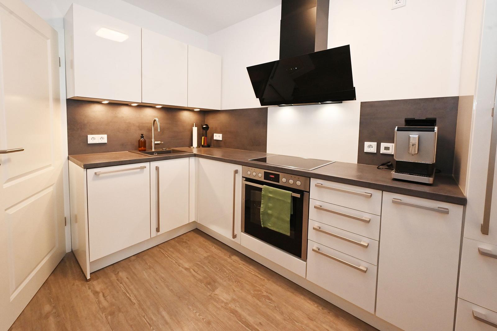 Moderne Küche mit weißen Schränken, dunkler Arbeitsplatte und integriertem Herd.