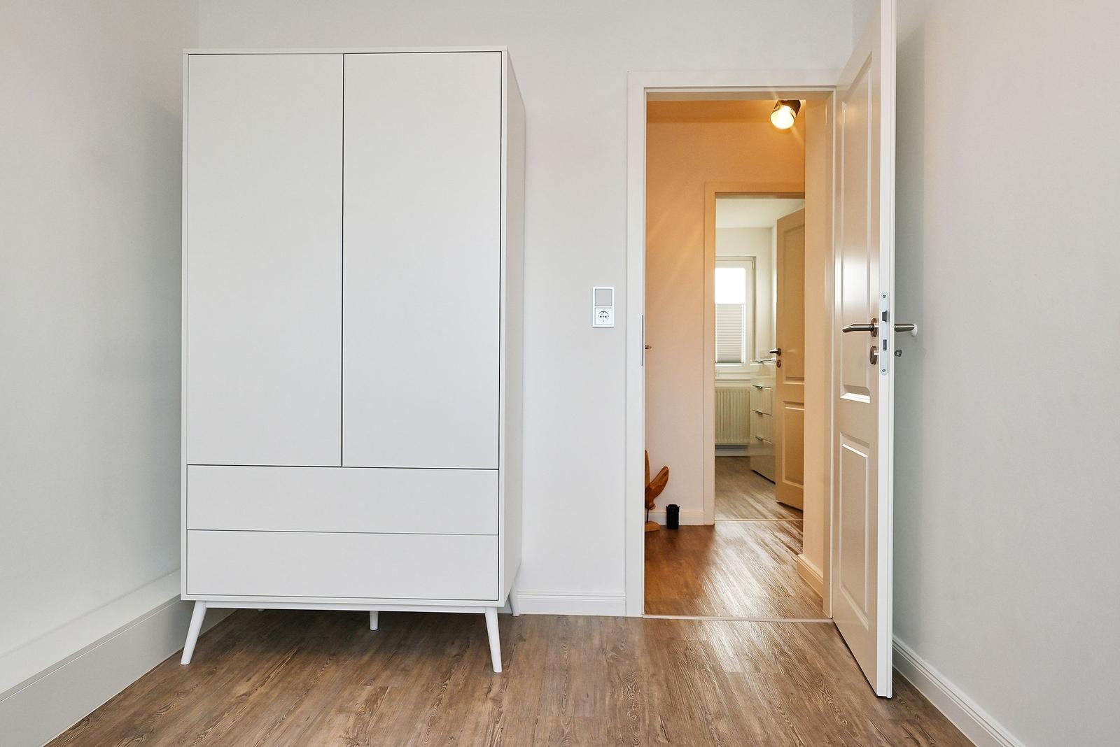 Schlafzimmer mit weißem Schrank und Tür zum Flur.