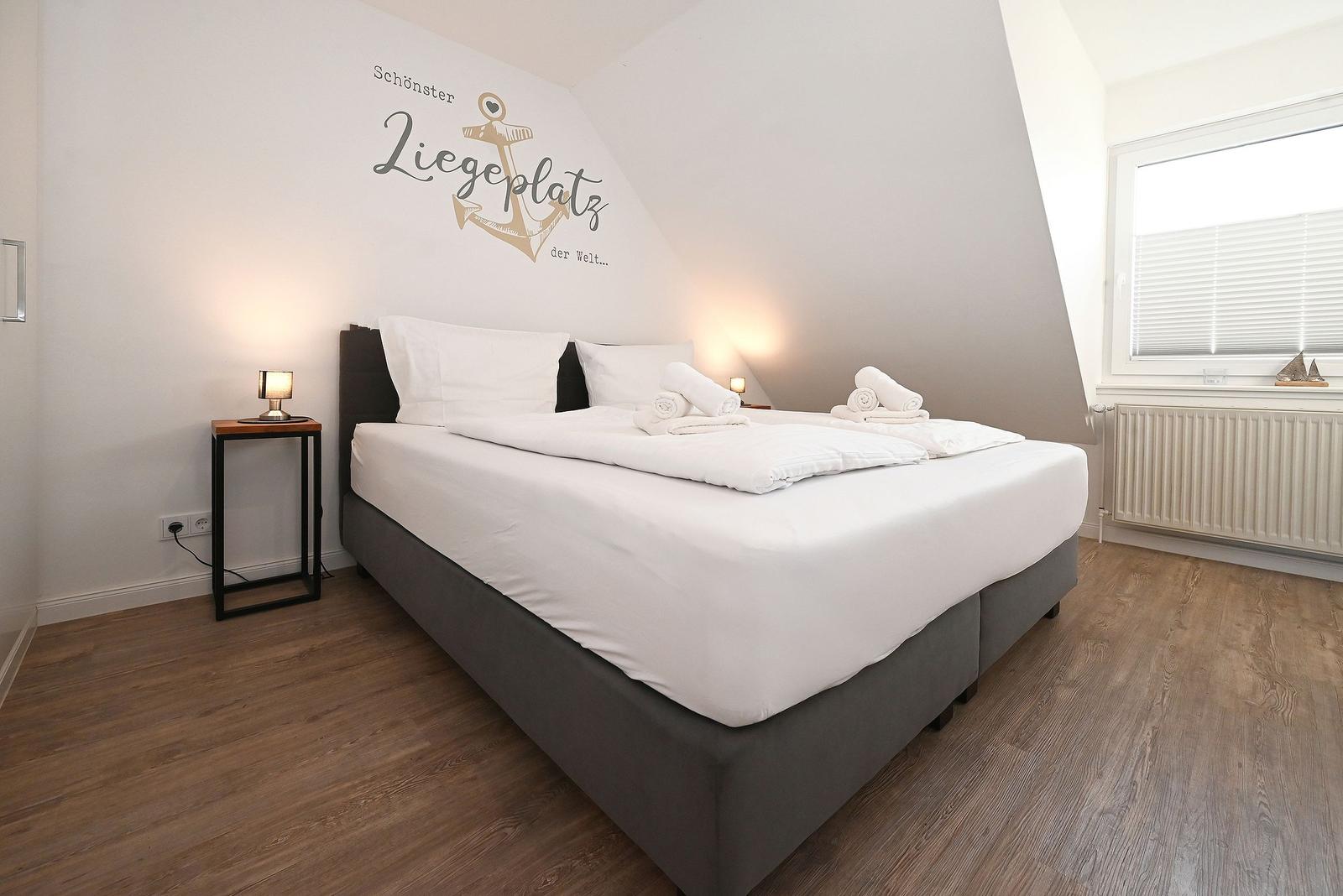 Schlafzimmer mit Bett, Wanddekoration und Fenster mit Jalousie.