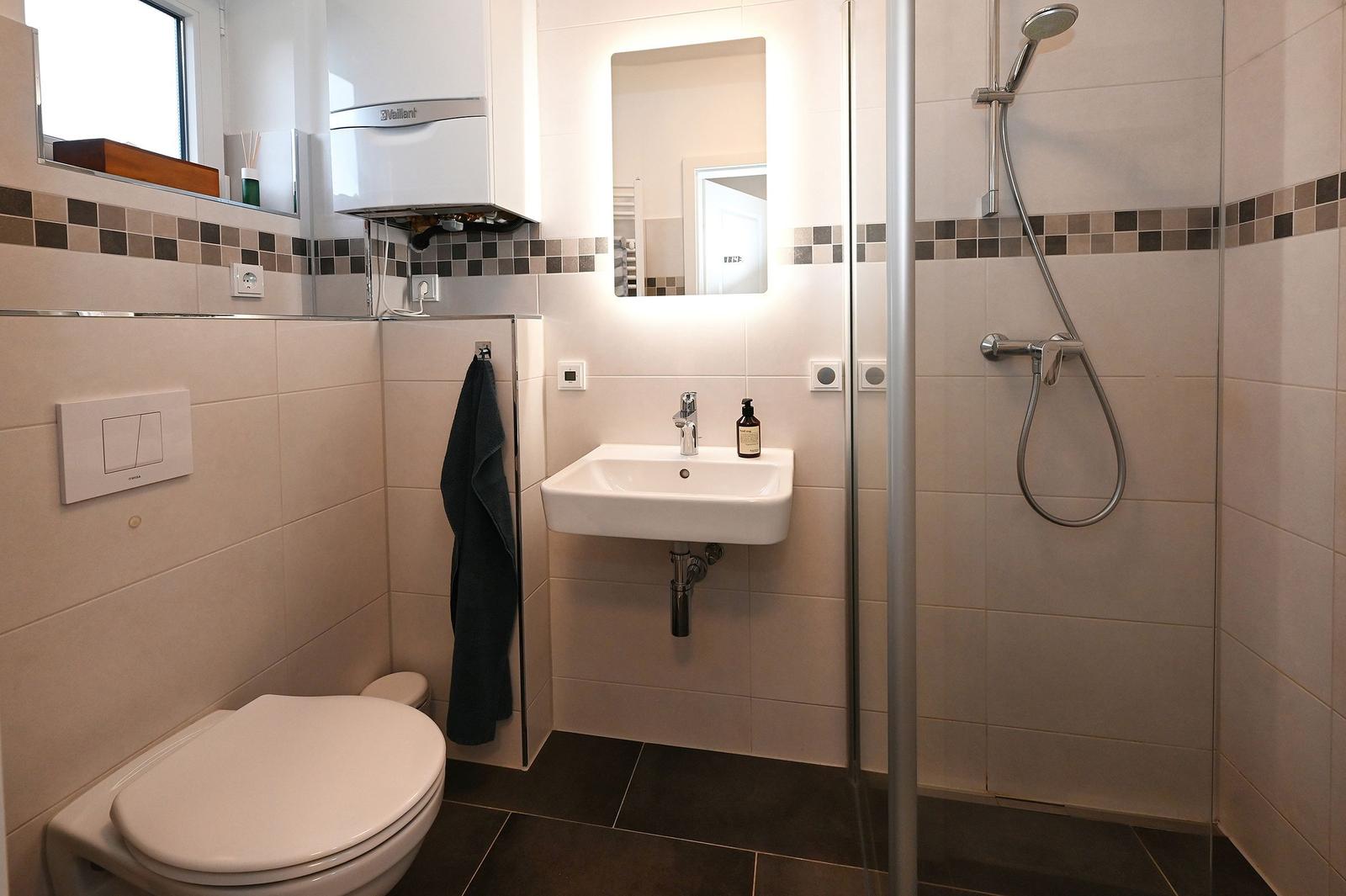 Badezimmer mit Dusche, Waschbecken und Toilette. Fliesen und Spiegel sichtbar.