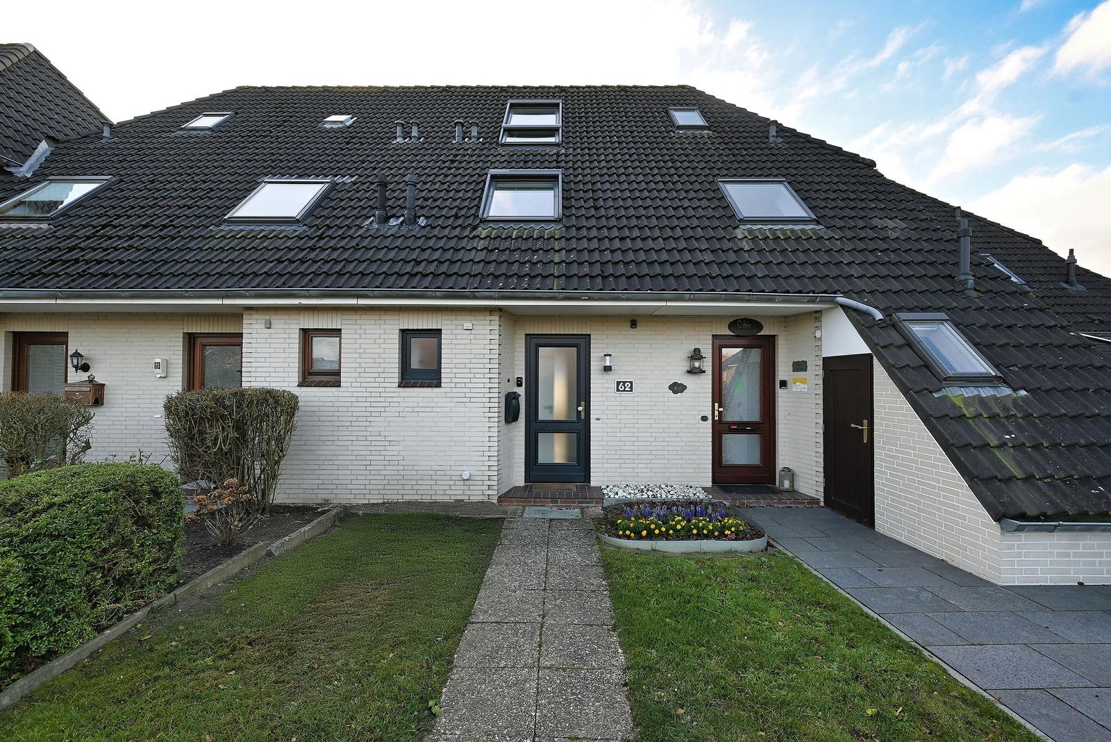 Einfamilienhaus mit Dachgauben, weißen Wänden und Vorgarten mit Blumenbeet.