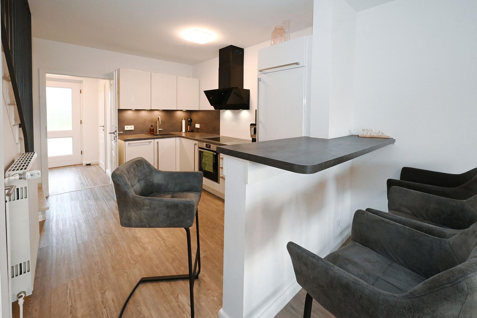 Küche mit Essbereich, grauen Barhockern und Holzboden.