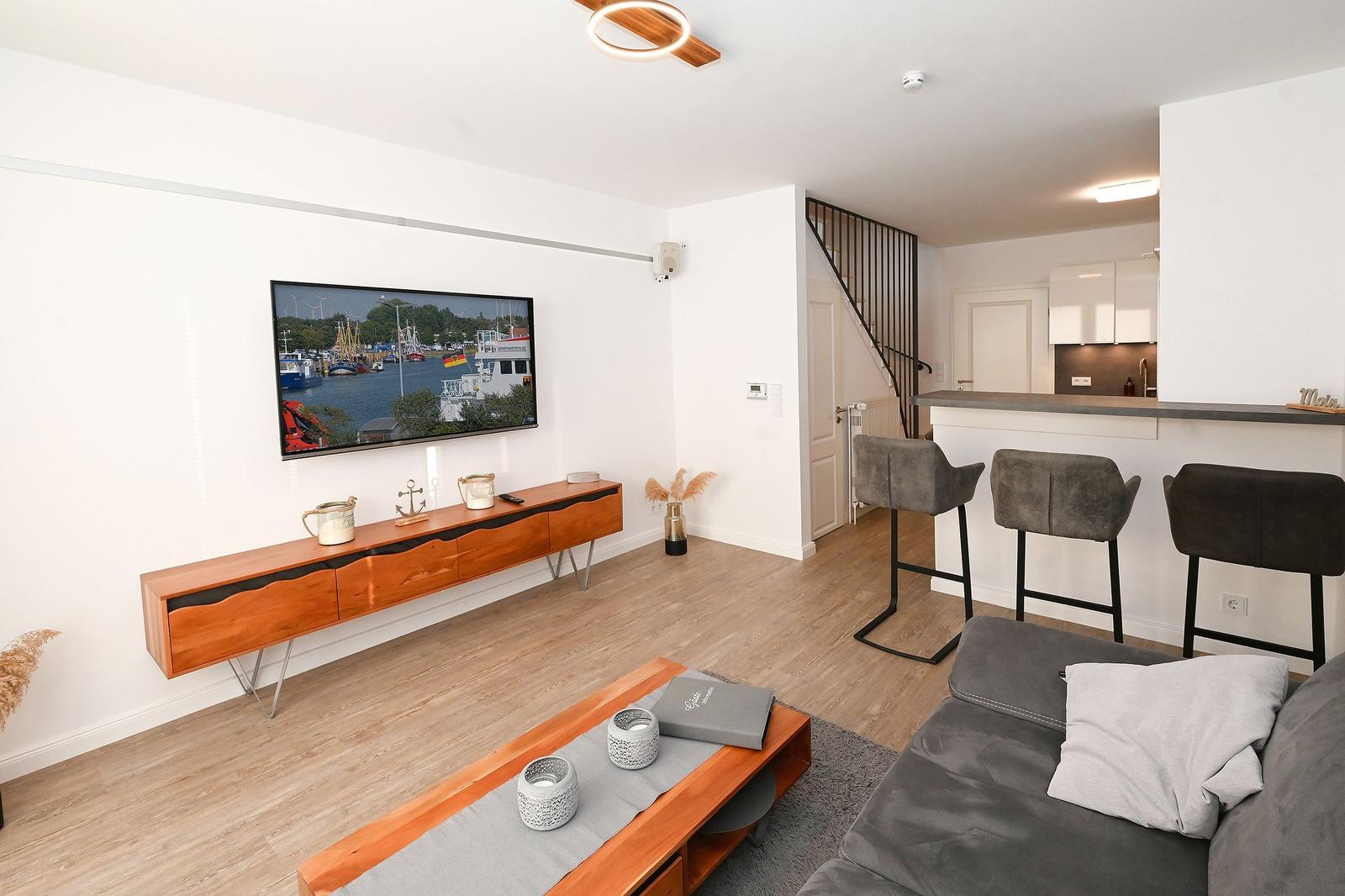 Wohnbereich mit TV, Sofa und Küchenbereich mit Barhocker.