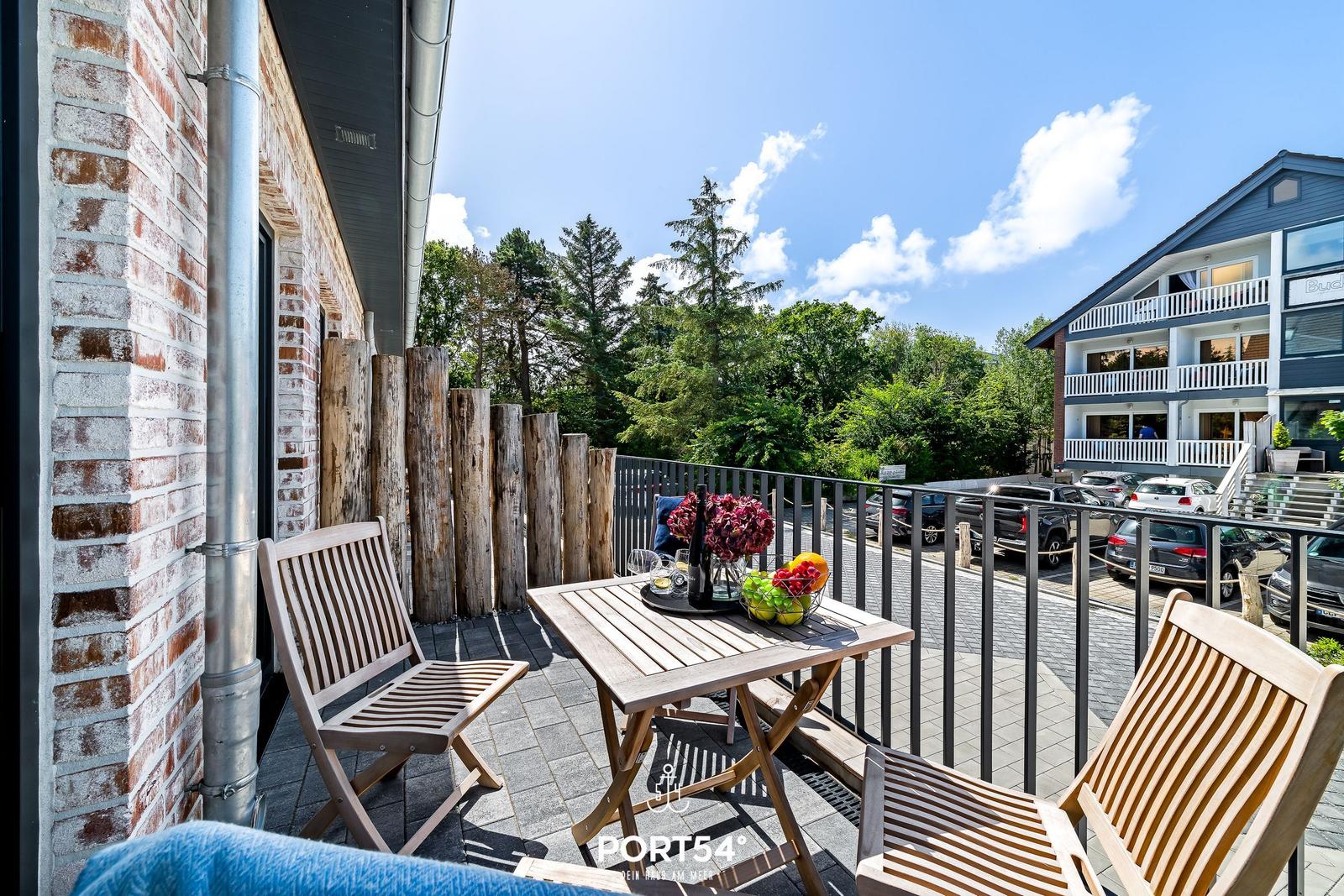Terrasse mit Holztisch und Stühlen, Blick auf grüne Bäume und benachbarte Gebäude.