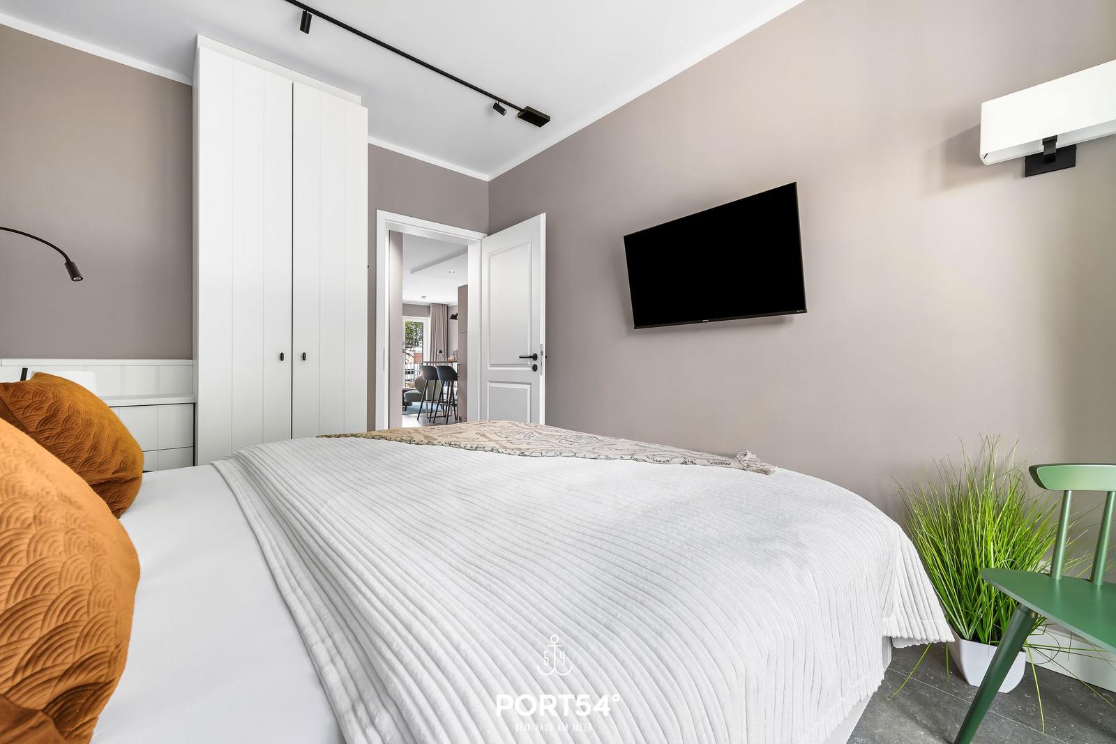 Schlafzimmer mit Bett, Kleiderschrank und Fernseher an der Wand.