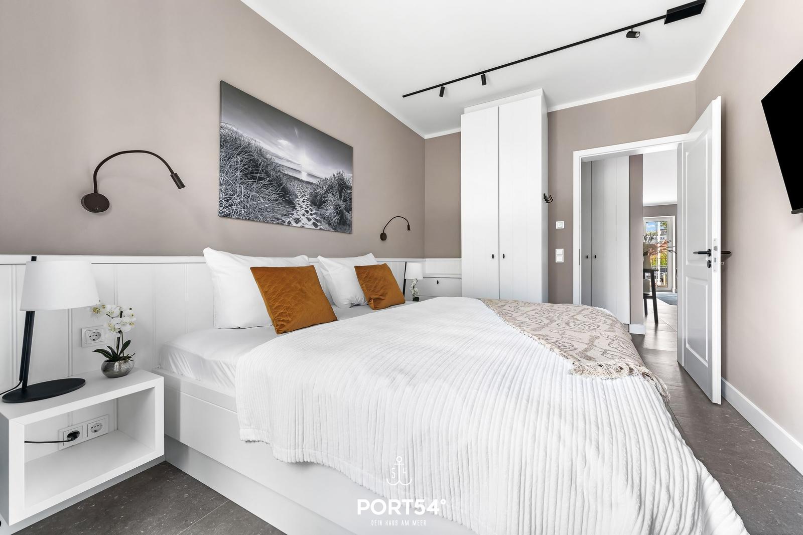 Schlafzimmer mit weißem Bett, Wandbild und Schwebetüren.