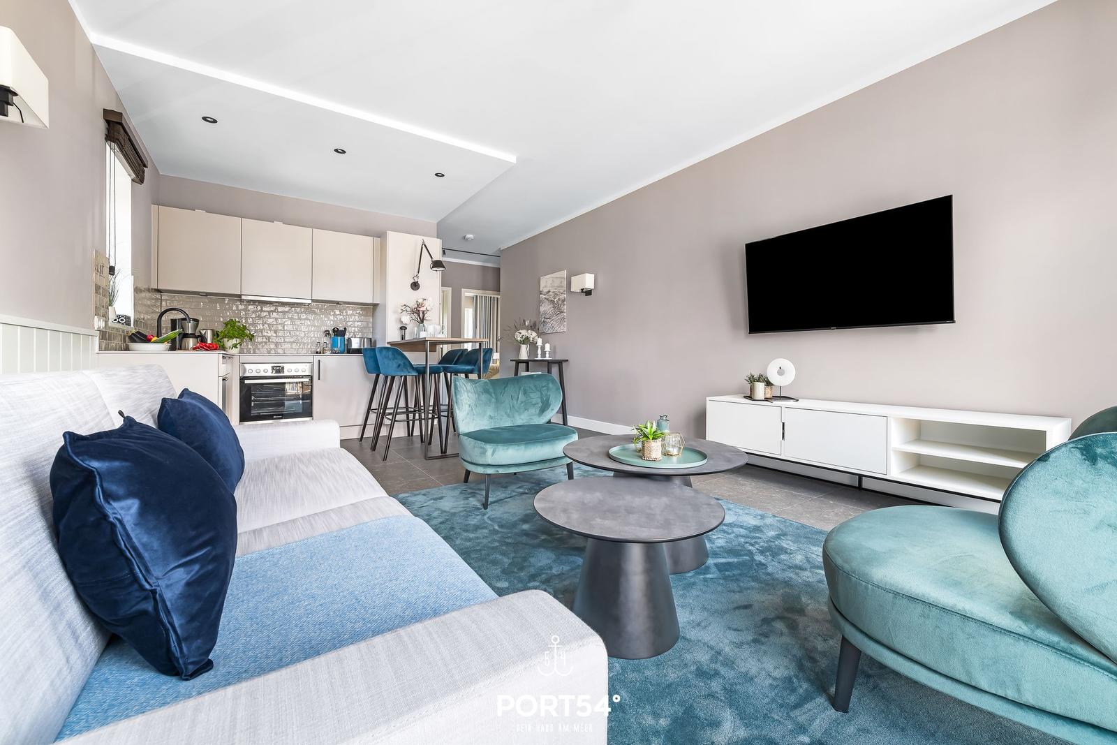 Wohnbereich mit Sofa, Sessel und Küchenbereich. Fernseher an der Wand.