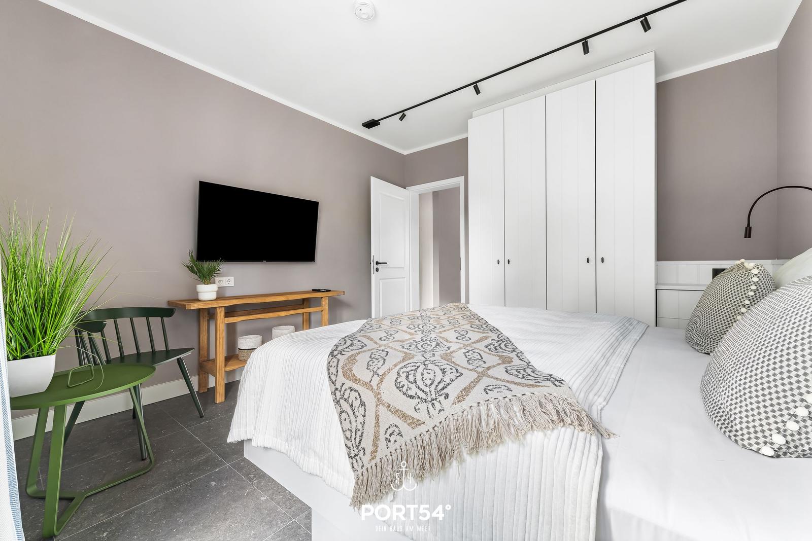 Schlafzimmer mit Bett, Kleiderschrank, Fernseher und Pflanzen.