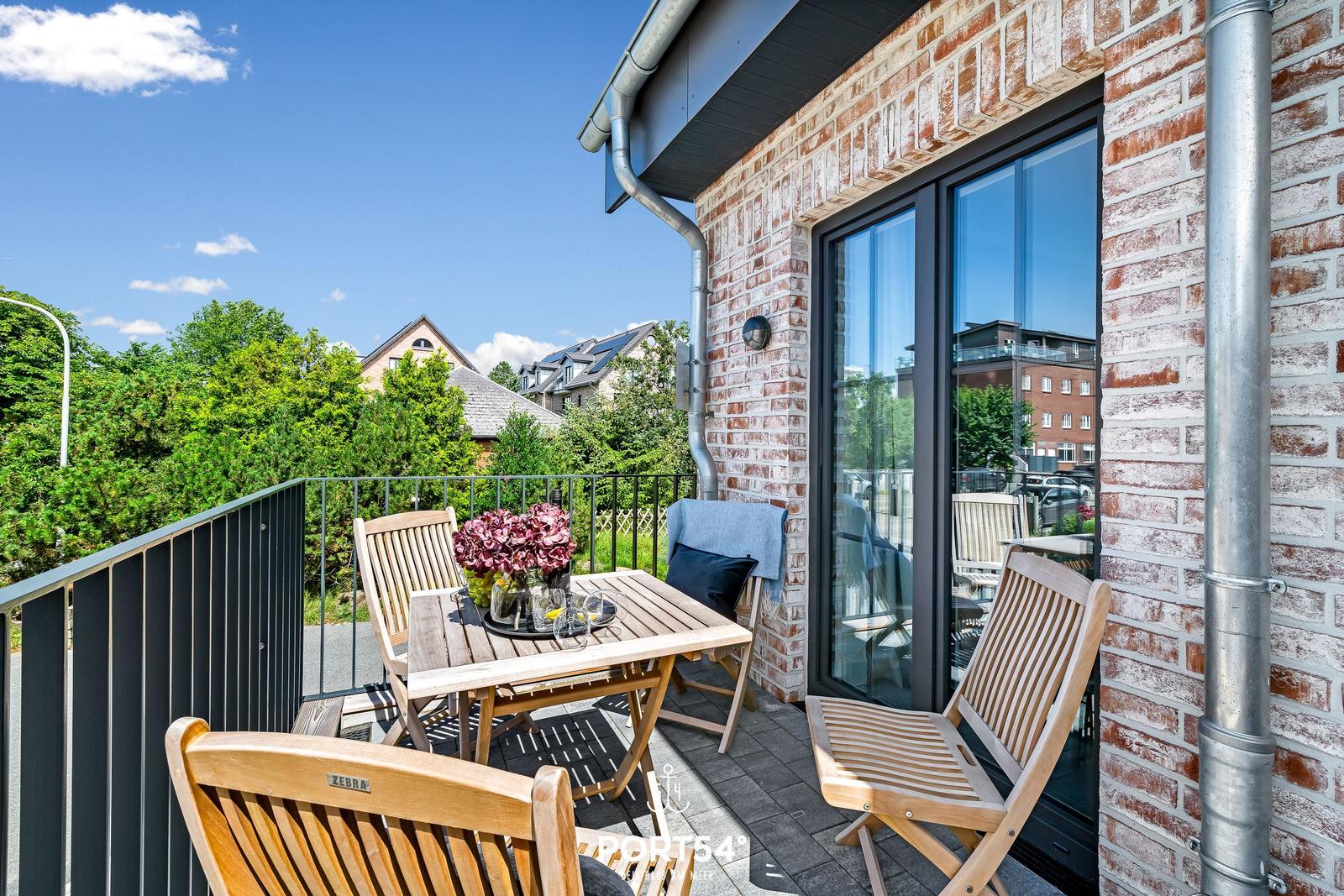 Terrasse mit Holztisch und Stühlen, Blick auf Grünflächen und Gebäude.