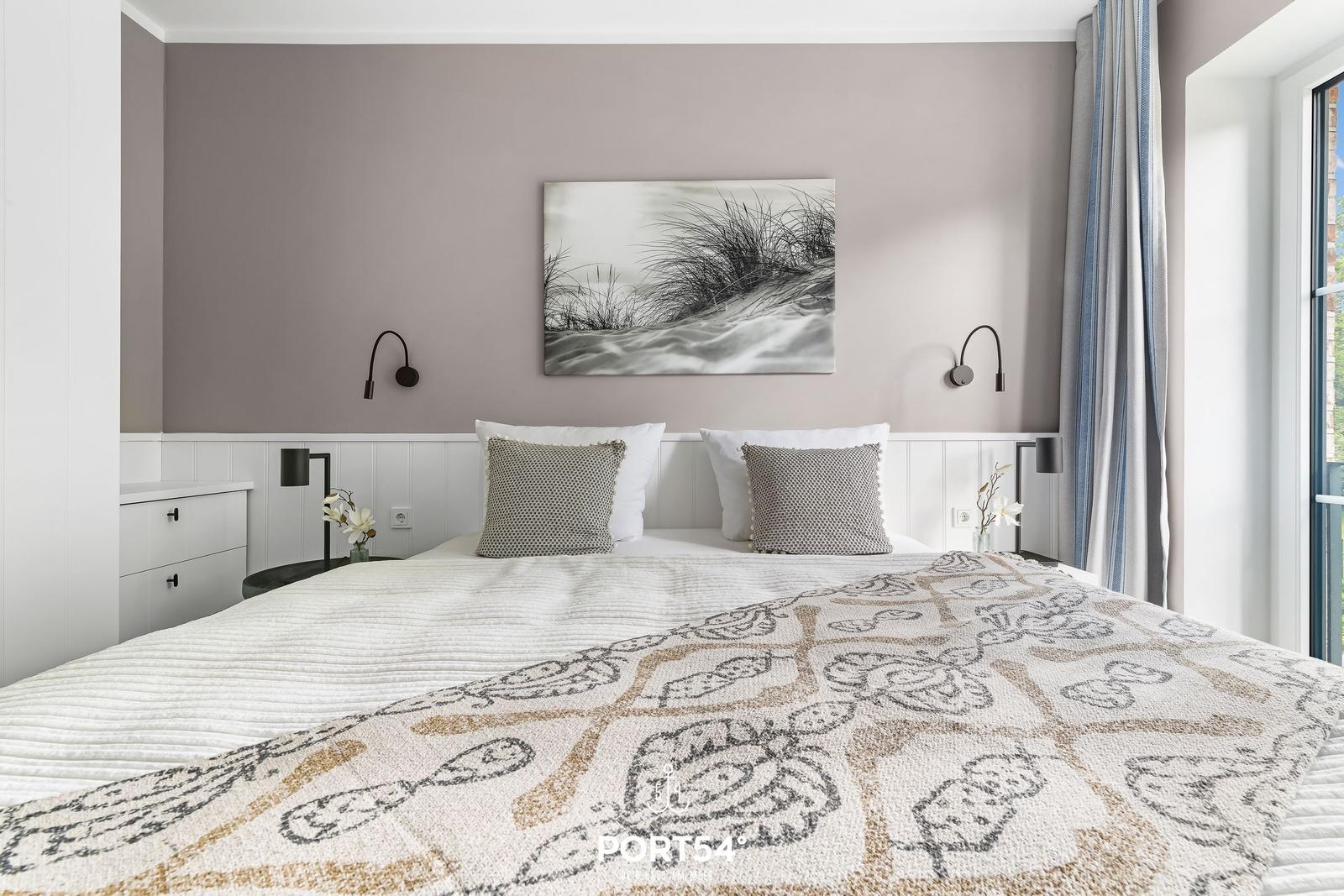 Schlafzimmer mit Bett, Wandbild und Fenster. Helle Einrichtung mit grauen und weißen Akzenten.