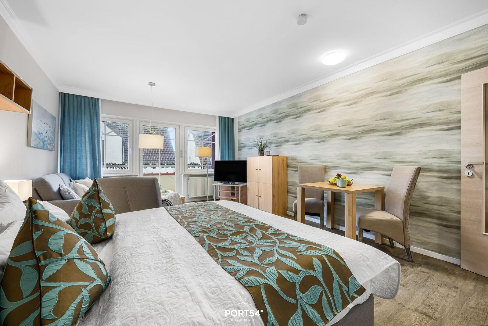 Schlafzimmer mit Bett, Sofa, TV und Esstisch. Wandtapete und Holzmöbel.