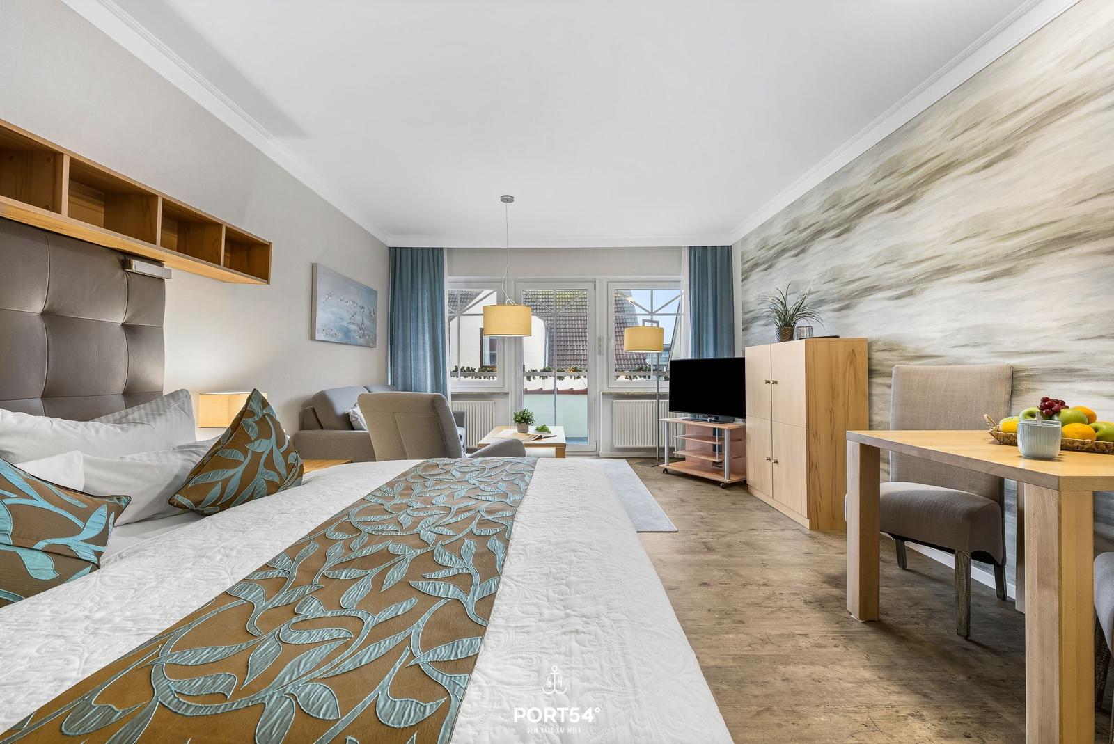 Schlafzimmer mit Bett, Sofa, Fernseher und Esstisch. Wand mit Muster, Fenster mit Blick.