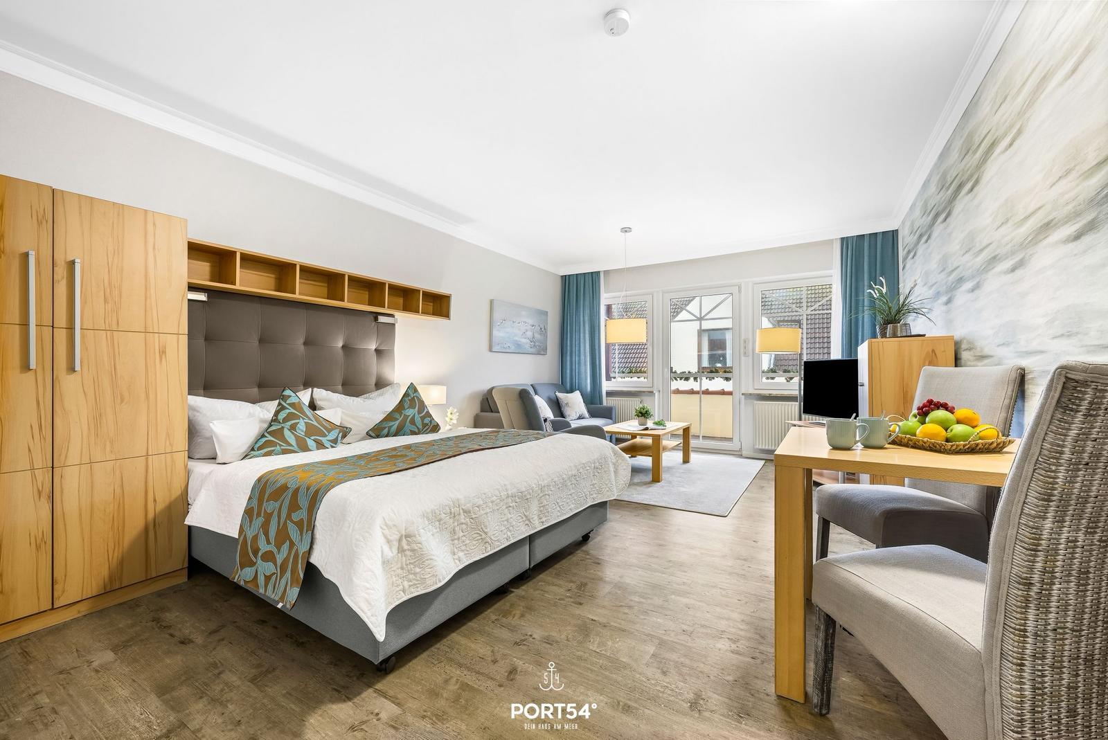 Schlafzimmer mit Bett, Wohnbereich und Essplatz. Holzboden und große Fenster.