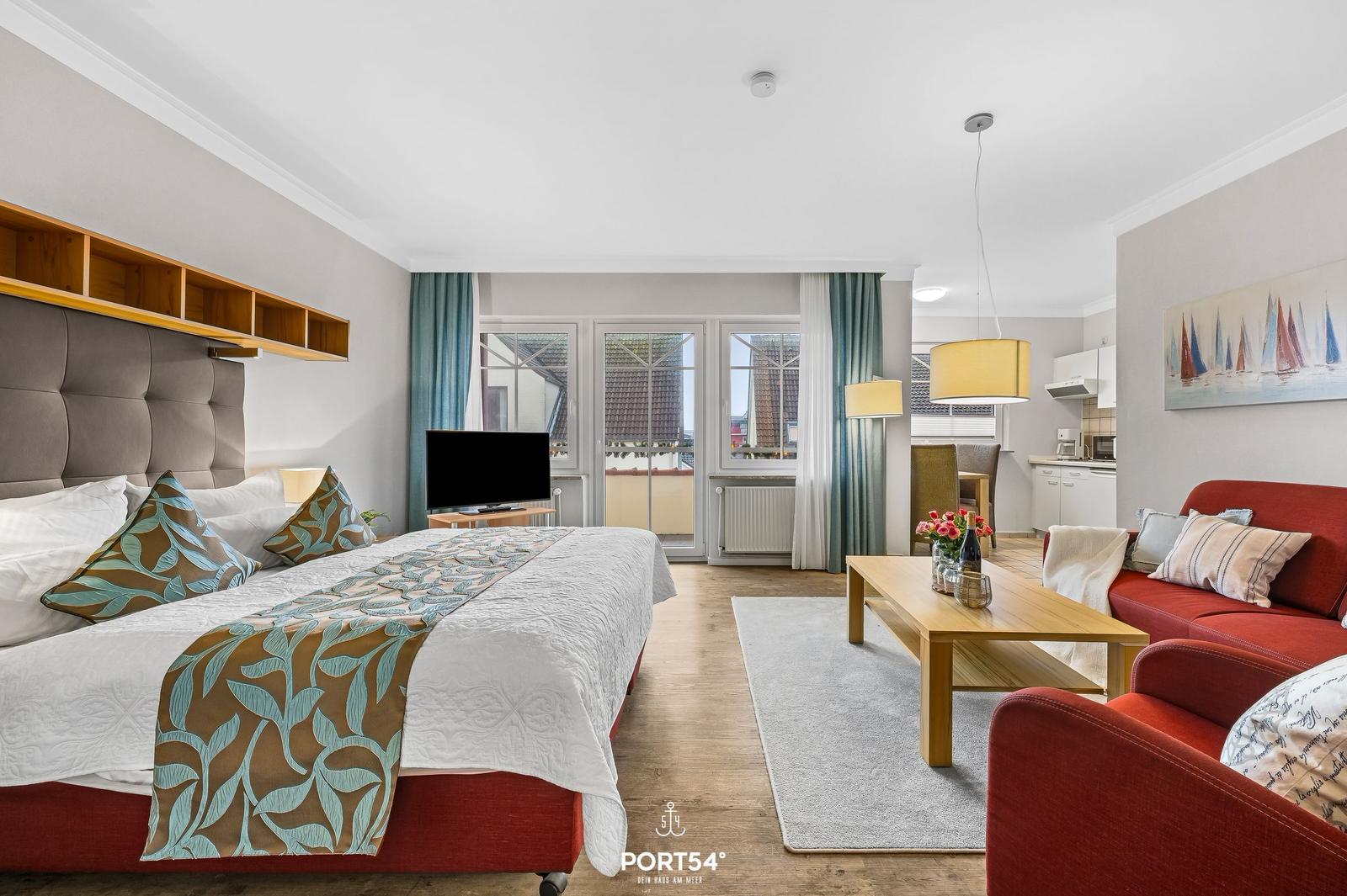 Schlafzimmer mit Bett, Wohnbereich mit Sofa und Küchenzeile. Balkon mit Blick auf Dächer.