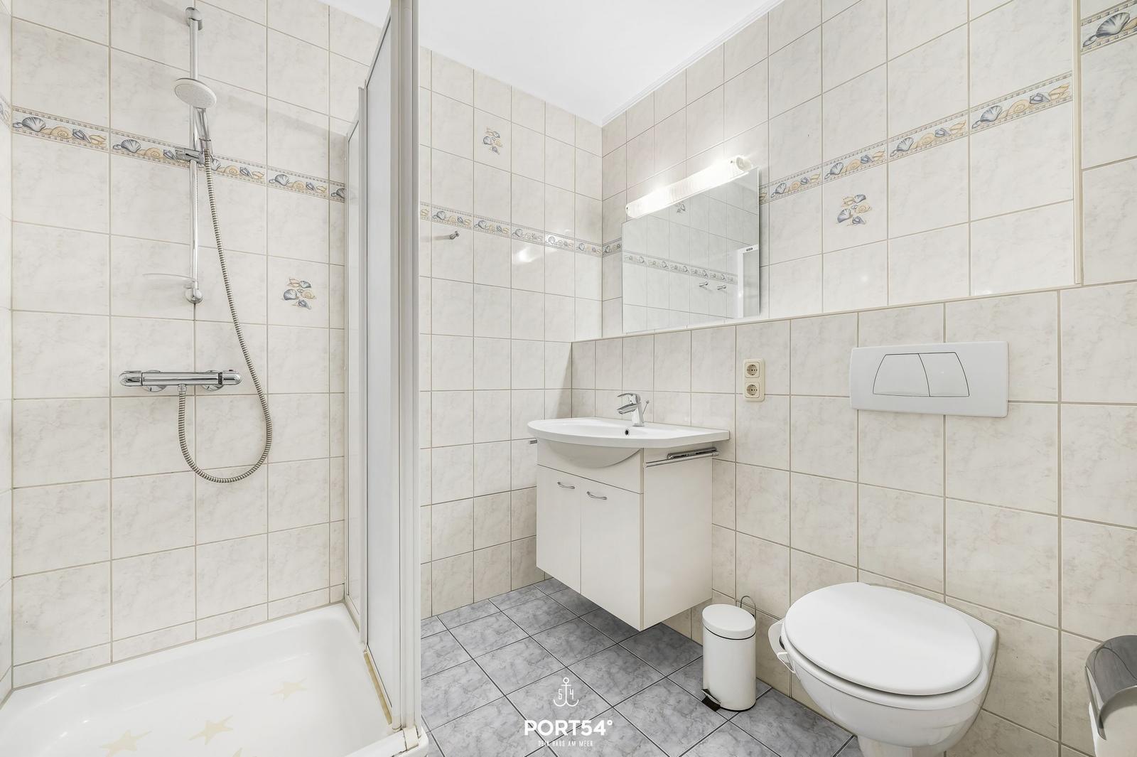 Badezimmer mit Dusche, Waschbecken und WC. Fliesen mit Muschel-Motiv.