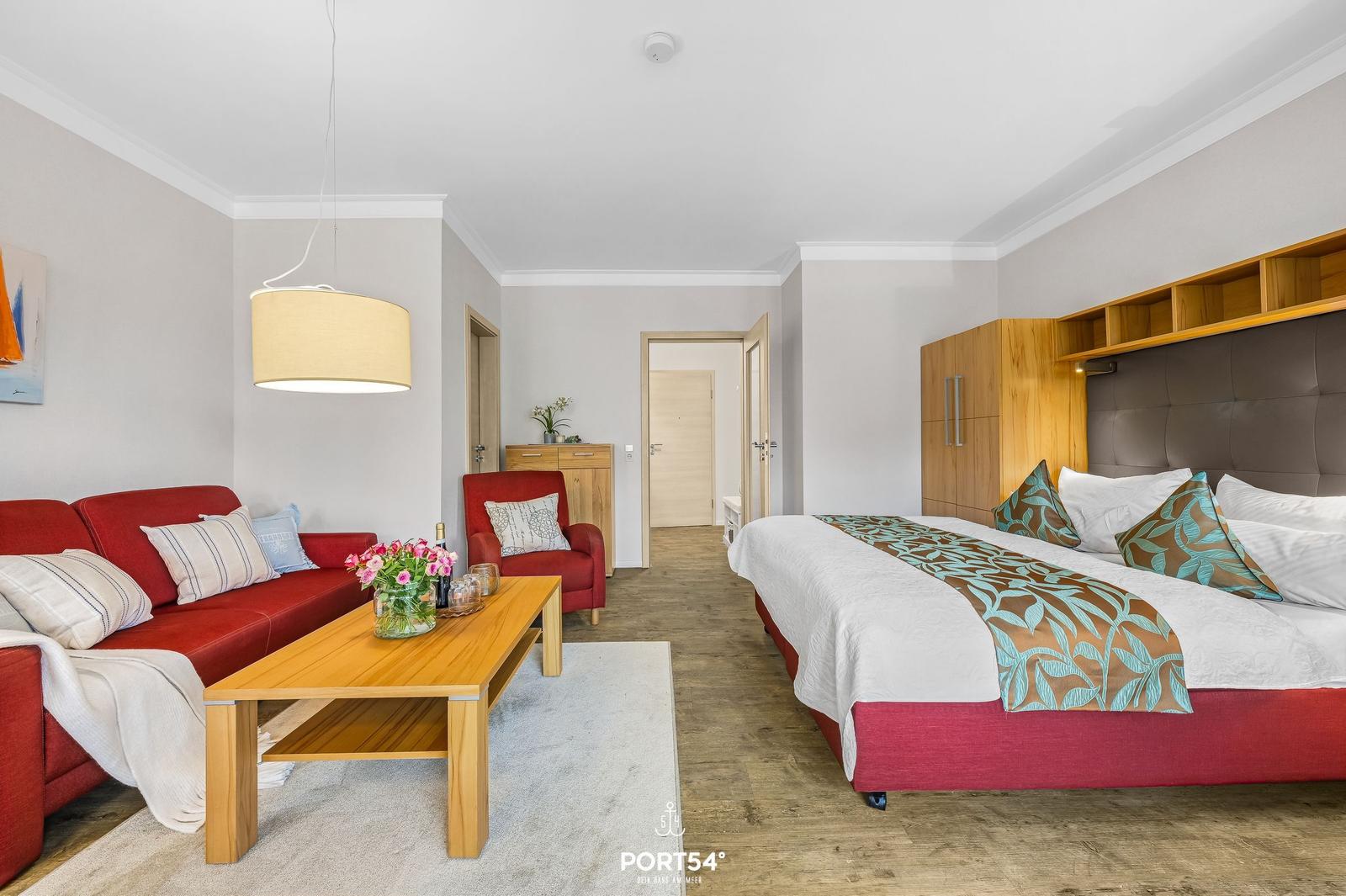 Ein Schlafzimmer mit rotem Sofa, Holztisch und Bett mit Muster.