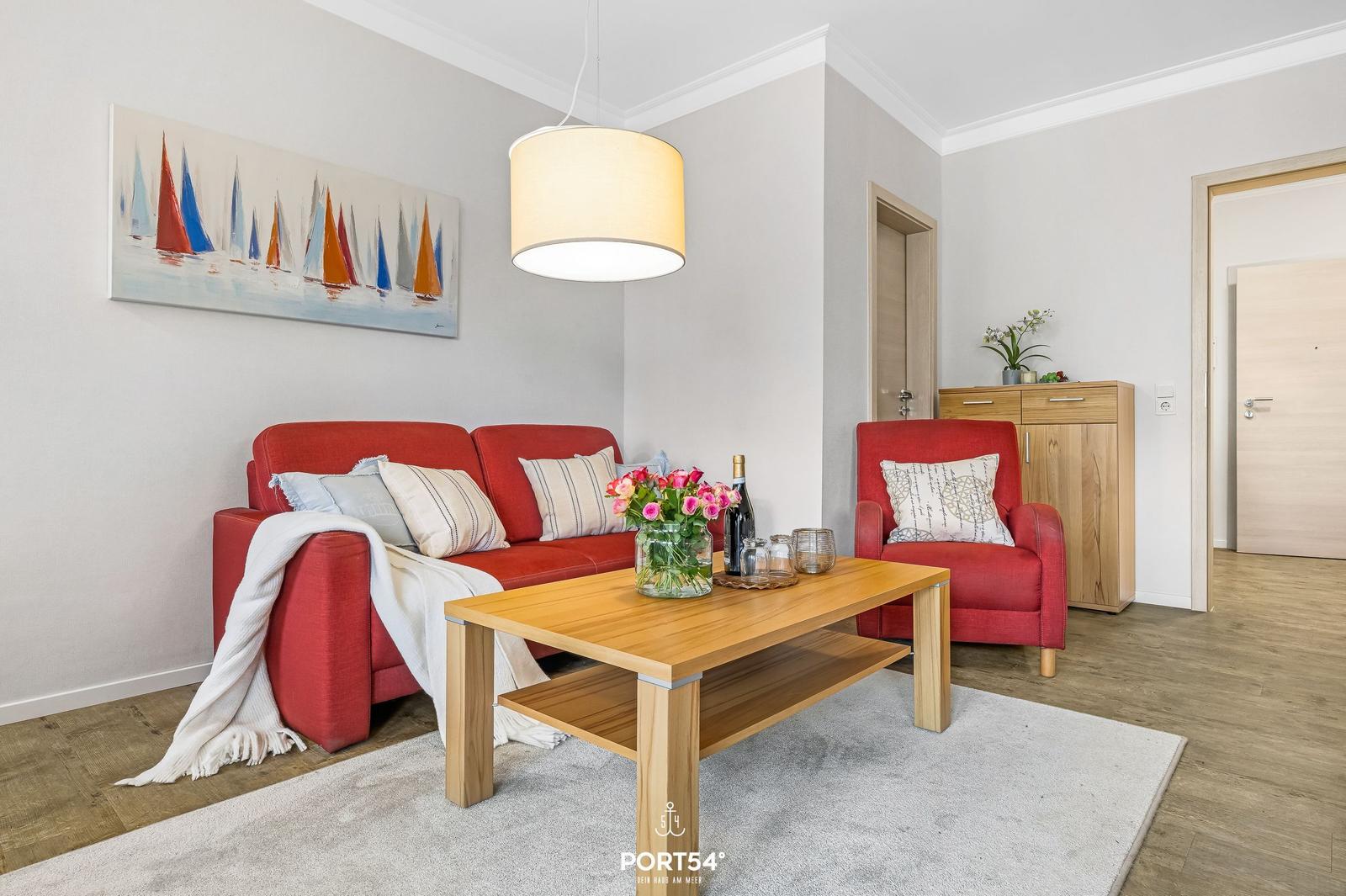 Ein Wohnzimmer mit rotem Sofa, Holztisch und Wandbild mit Segelbooten.
