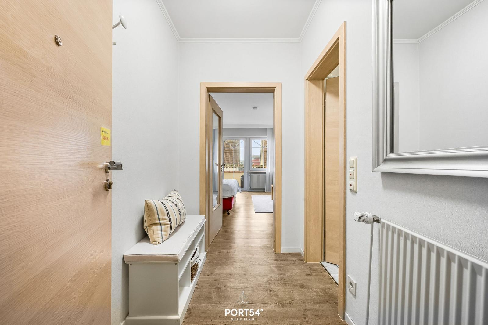 Flur mit Sitzbank, Spiegel und Blick in Schlafzimmer mit Fenster.