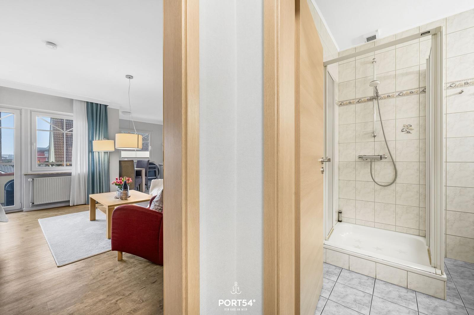 Badezimmer mit Dusche und Blick in Wohnbereich mit Sofa und Tisch.