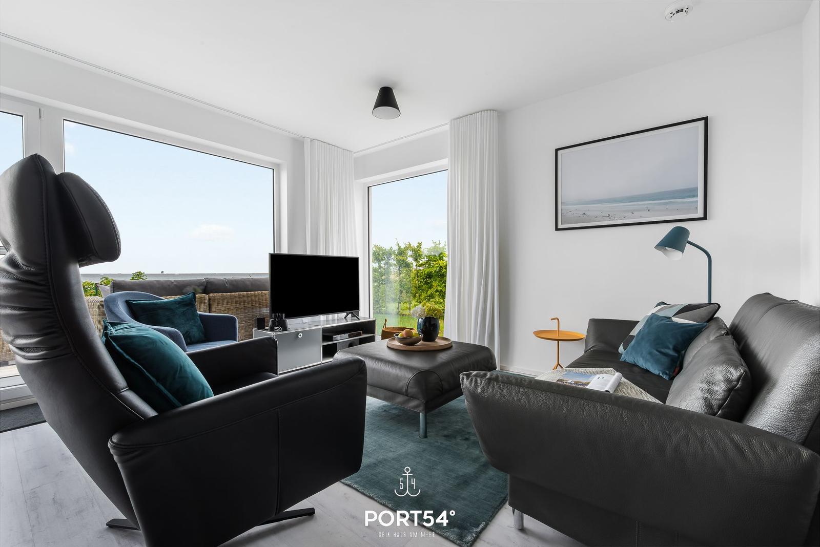 Wohnzimmer mit schwarzen Ledermöbeln, großen Fenstern und Blick aufs Meer.