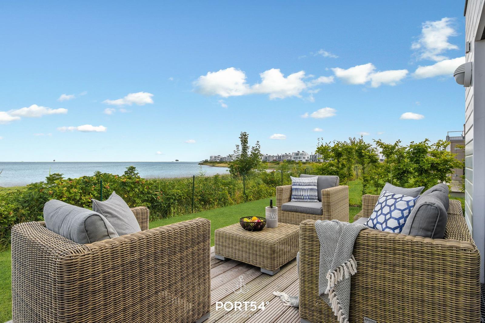 Terrasse mit Rattanmöbeln und Blick aufs Wasser.