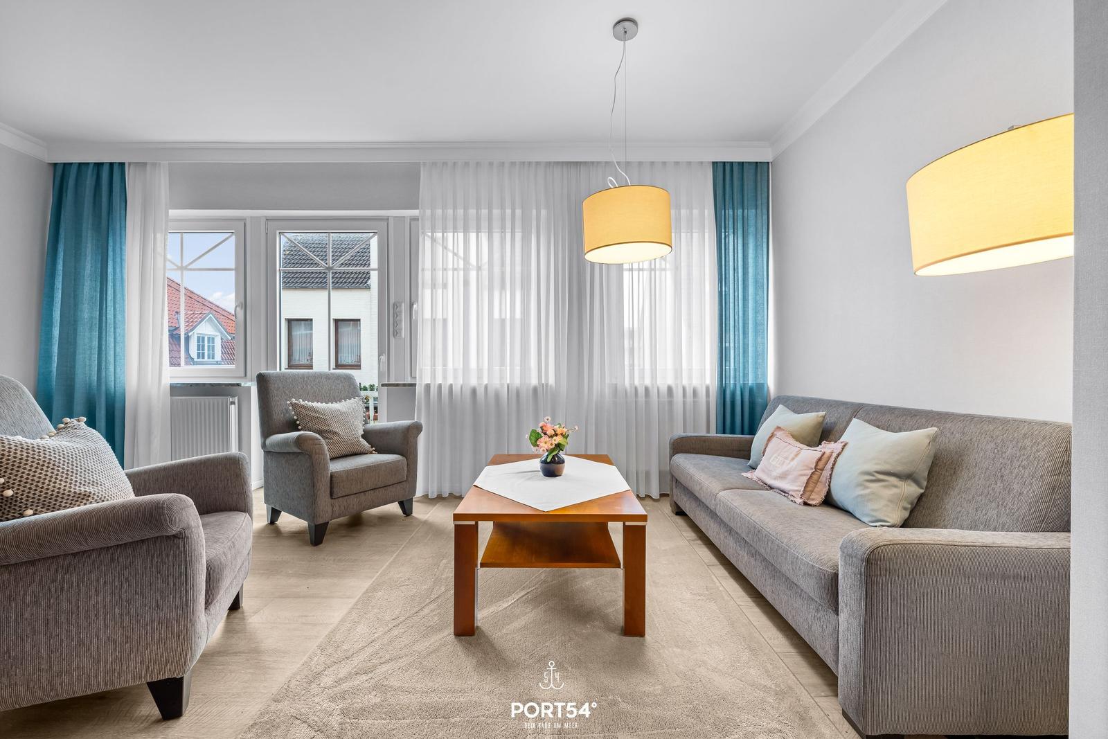 Wohnzimmer mit Sofa, Sessel und Tisch. Fenster mit Vorhängen und Deckenleuchten.