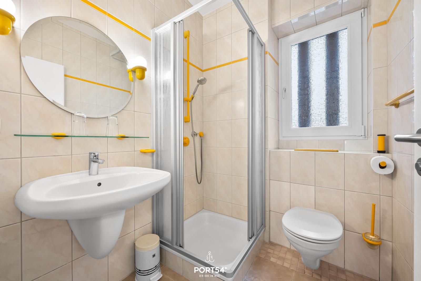 Bad mit Dusche, Waschbecken und Toilette. Gelbe Akzente an den Wänden.