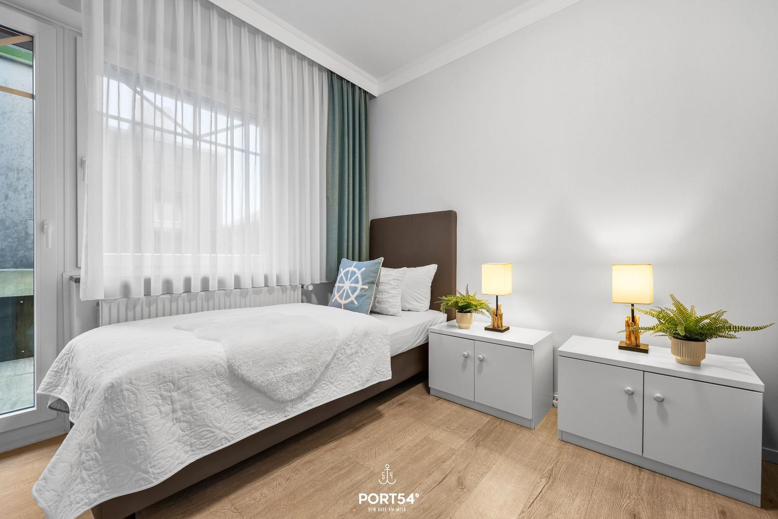 Schlafzimmer mit Bett, zwei Nachttischen und Fenster mit Vorhängen.