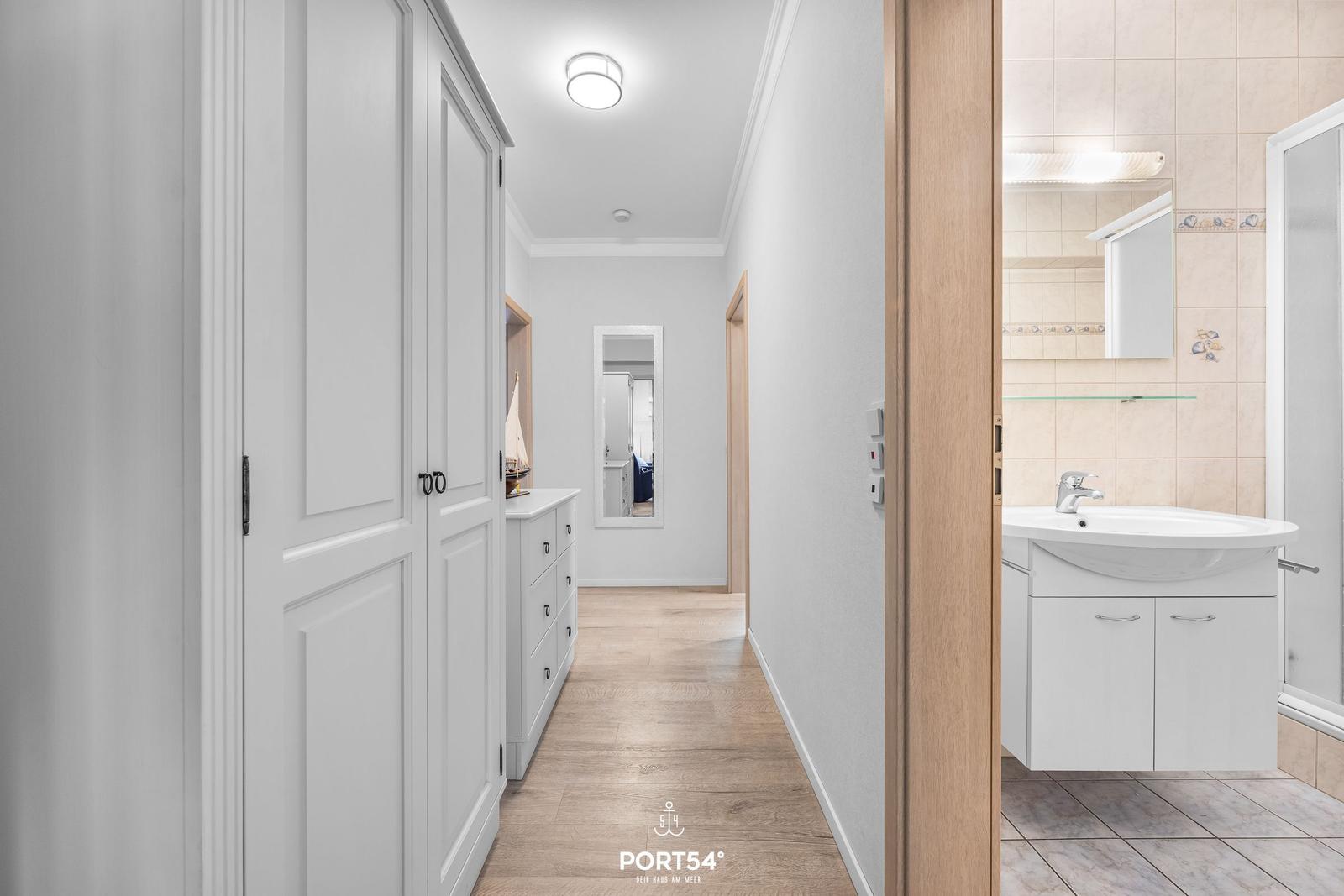 Flur mit Kleiderschrank und Blick in das Badezimmer mit Waschbecken und Spiegel.