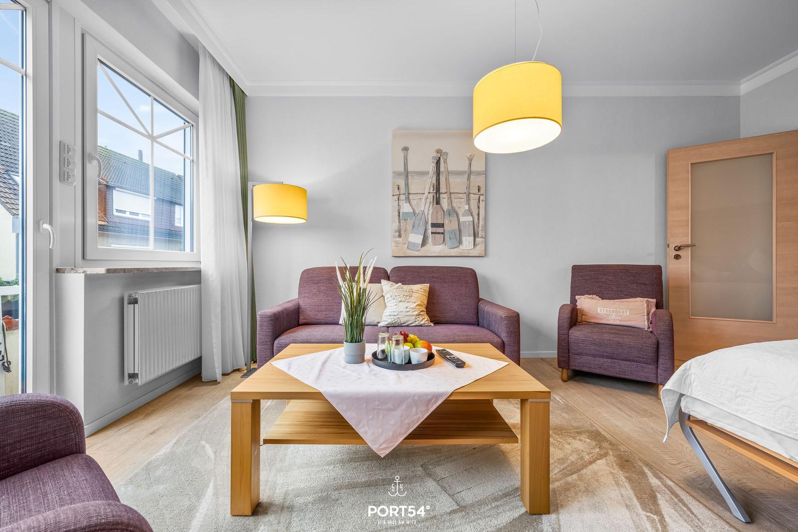 Wohnzimmer mit Sofa, Sessel und Tisch. Fenster, Wandbild und Bett sichtbar.