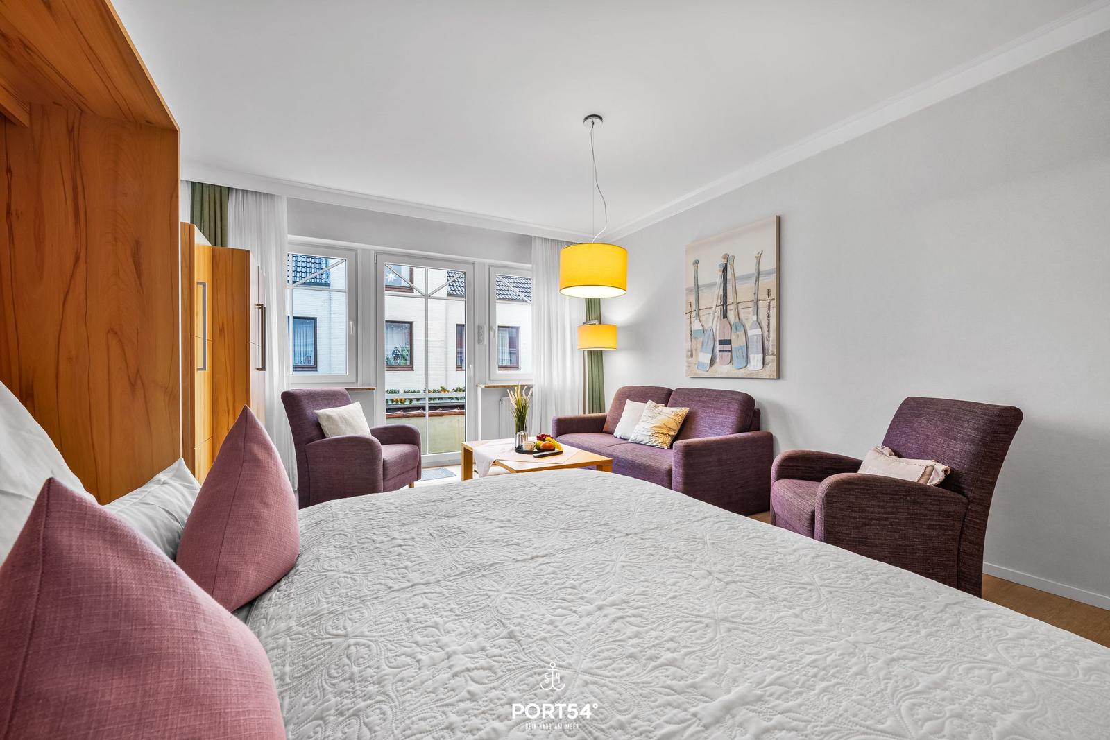 Schlafzimmer mit Doppelbett, Sitzgruppe und Balkonansicht.