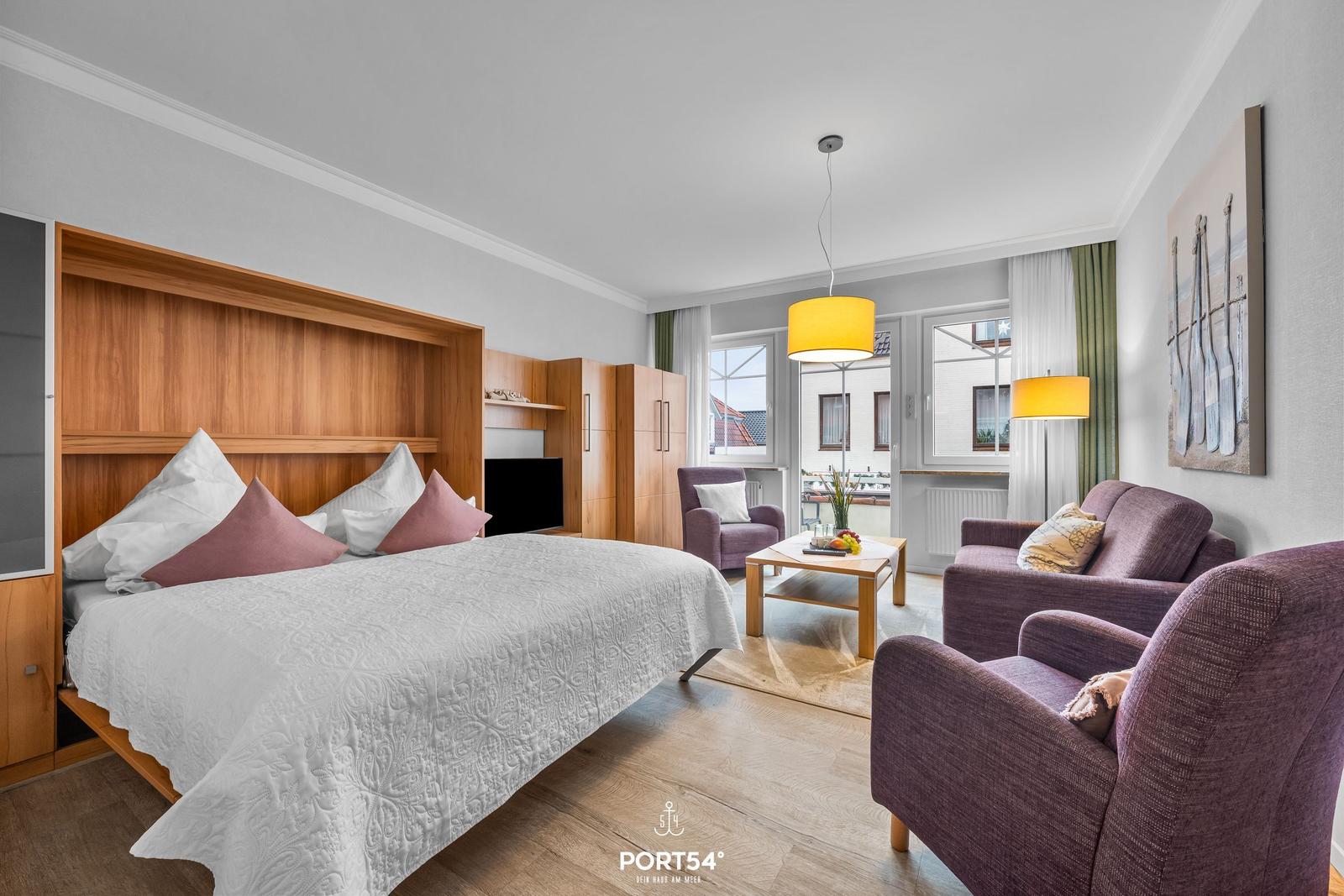 Schlafzimmer mit Bett und Wohnbereich mit Sitzgelegenheiten und Fenster.