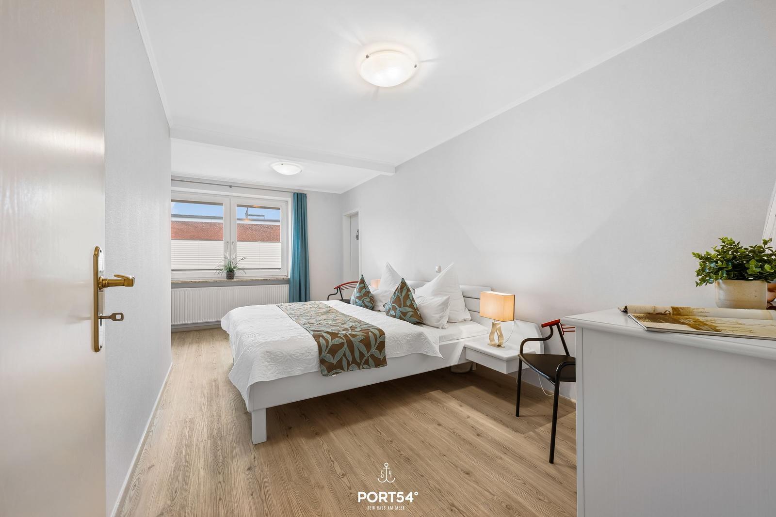 Schlafzimmer mit Bett, Nachttisch, Lampe und Fenster mit Blick.