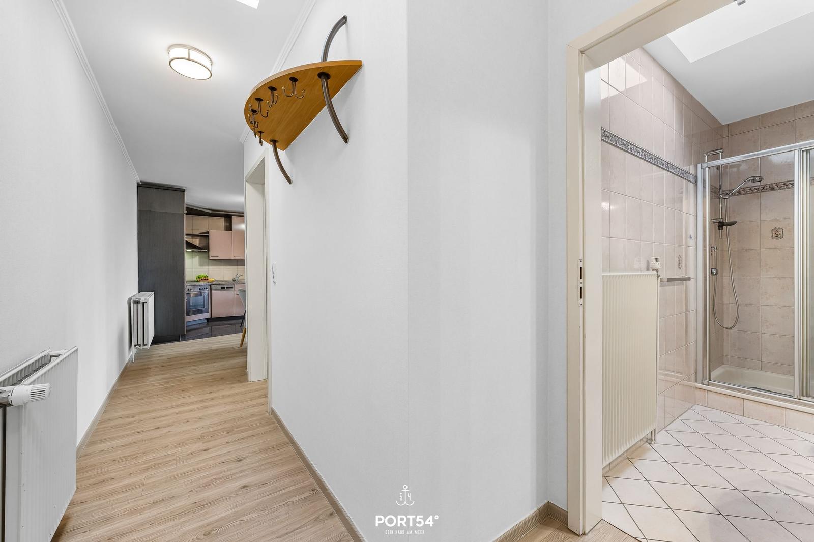 Flur mit Küchen- und Badezimmeransicht. Holzboden, Wandgarderobe und Dusche sichtbar.