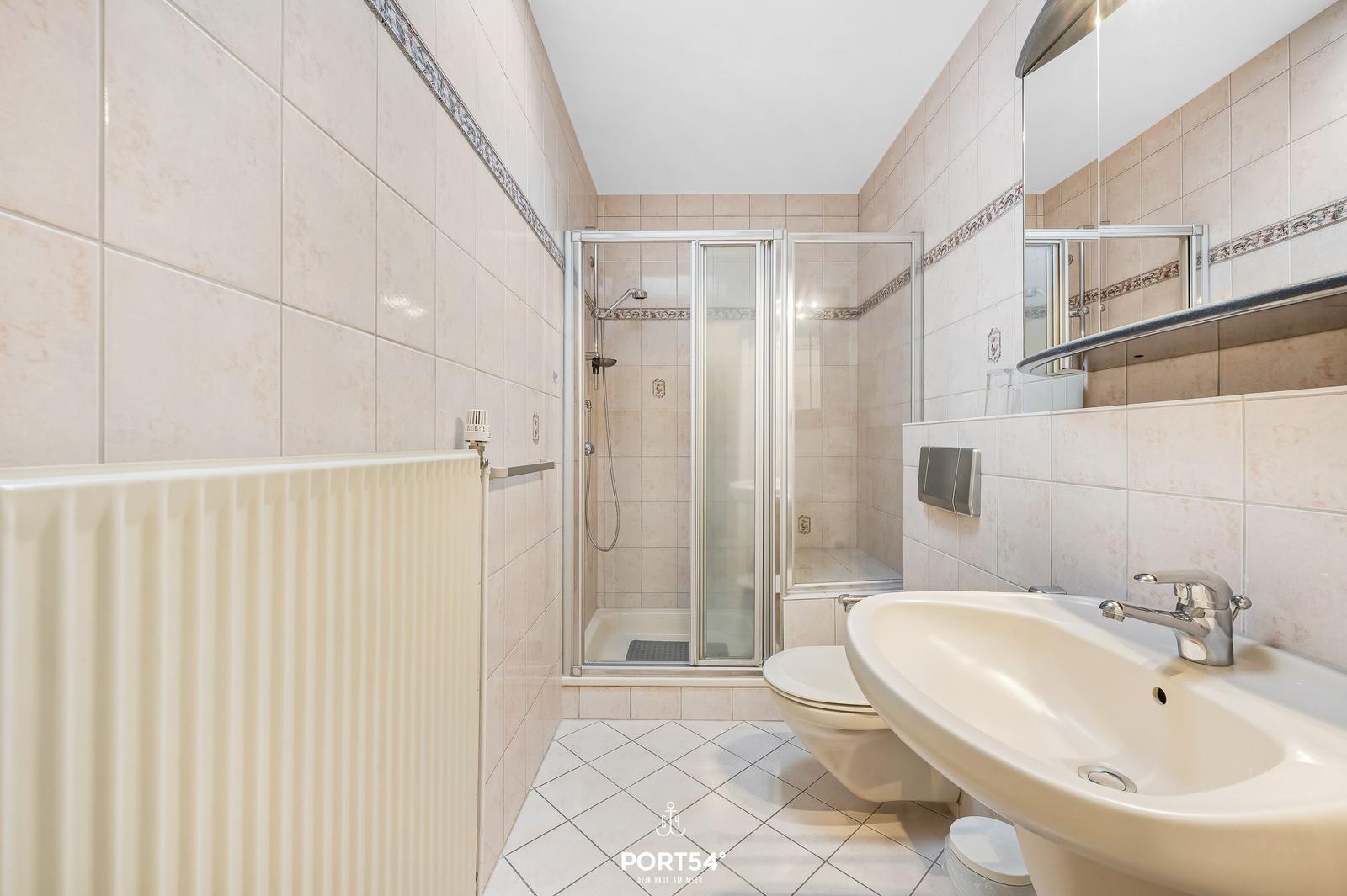 Bad mit Dusche, Waschbecken und Toilette. Fliesenwand und Boden.