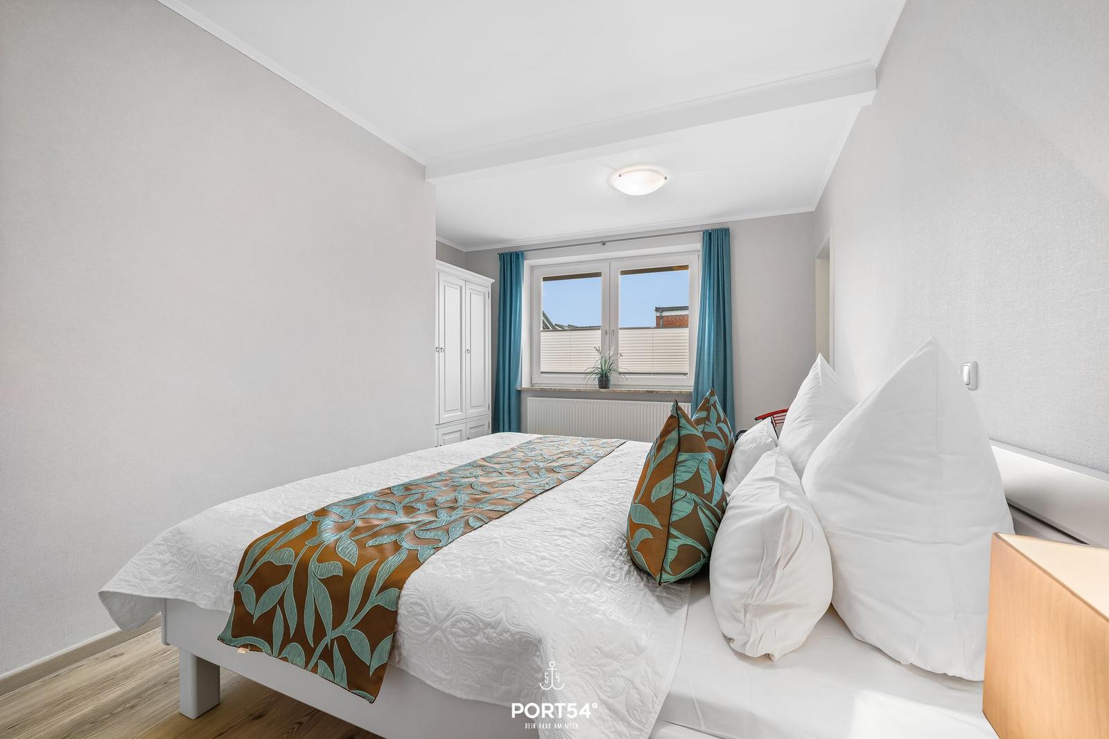 Schlafzimmer mit weißem Bett, blauen Vorhängen und Holzboden.