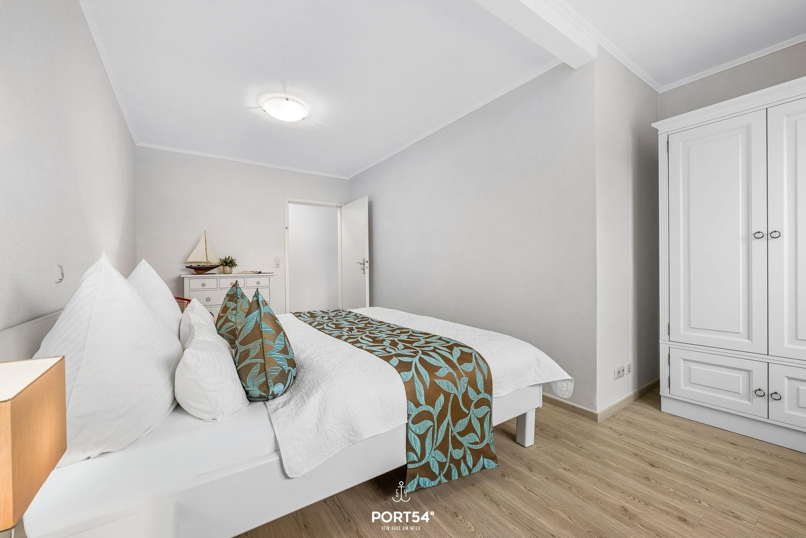 Schlafzimmer mit weißem Bett, Kleiderschrank und Holzboden