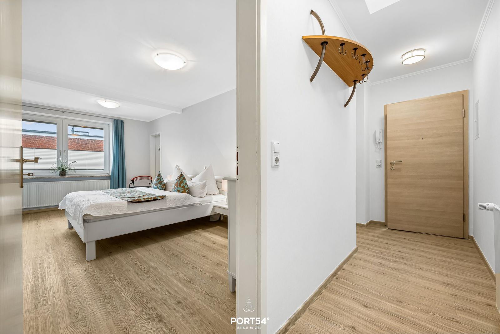 Schlafzimmer mit Bett und Fenster. Flur mit Tür und Wandhaken.