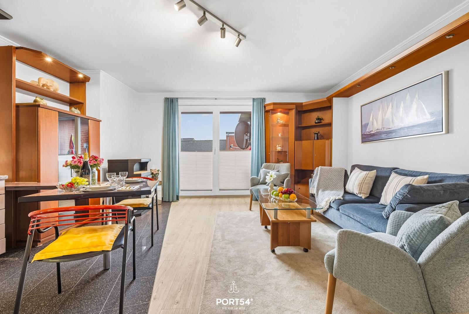 Wohn- und Essbereich mit Sofa, Tisch und Blick auf Balkon.