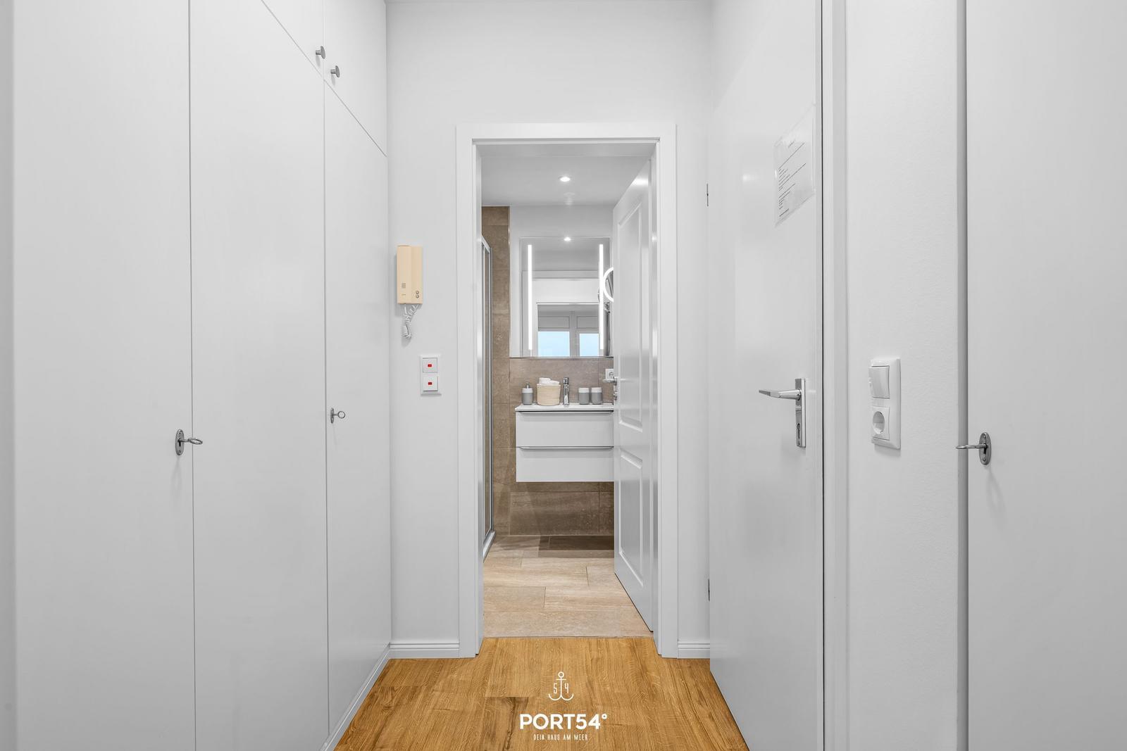 Flur mit Holzboden und Blick in das Badezimmer mit Waschbecken und Spiegel.